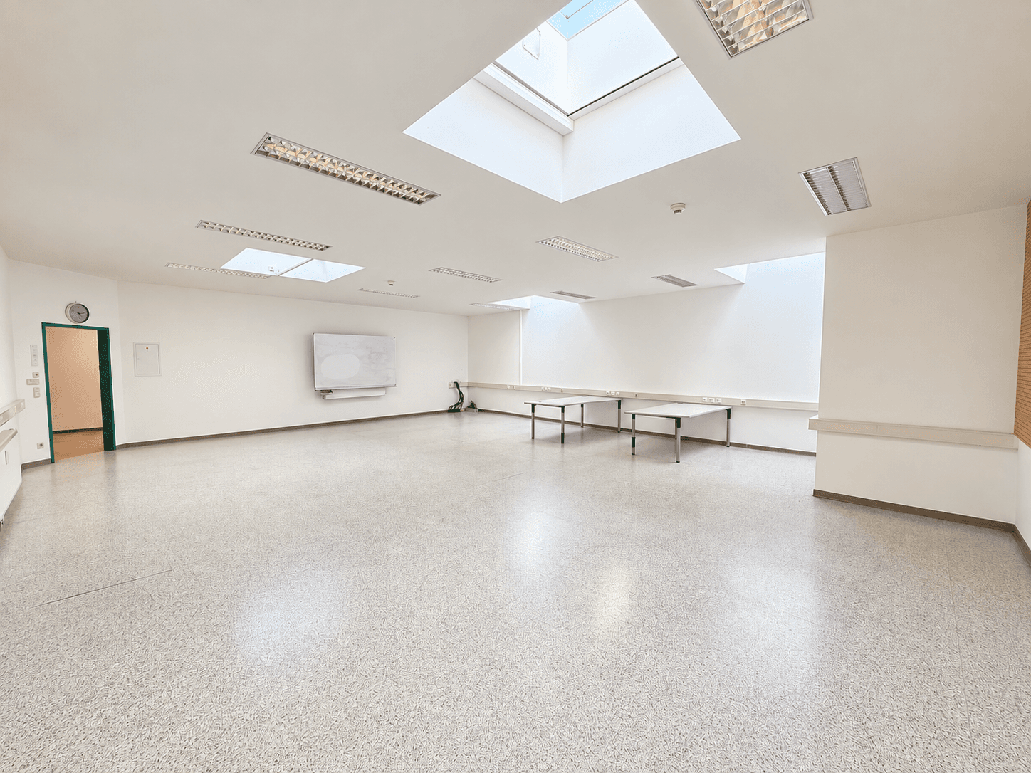 Großer, leerer Büroraum mit mehreren Oberlichtern, Whiteboards und einer Rasterdecke.