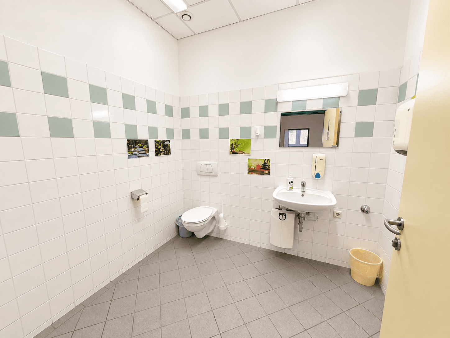 Öffentliche Toilette mit einem WC, Waschbecken und hell gefliesten Wänden und Böden.