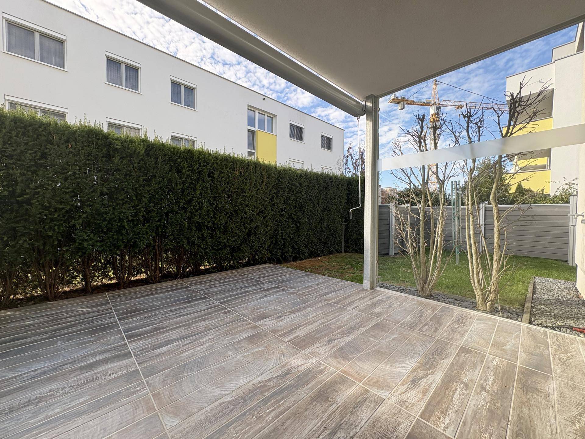 Geräumige geflieste Terrasse mit Hecke und kleinem Gartenbereich, ideal für Entspannung im Freien.