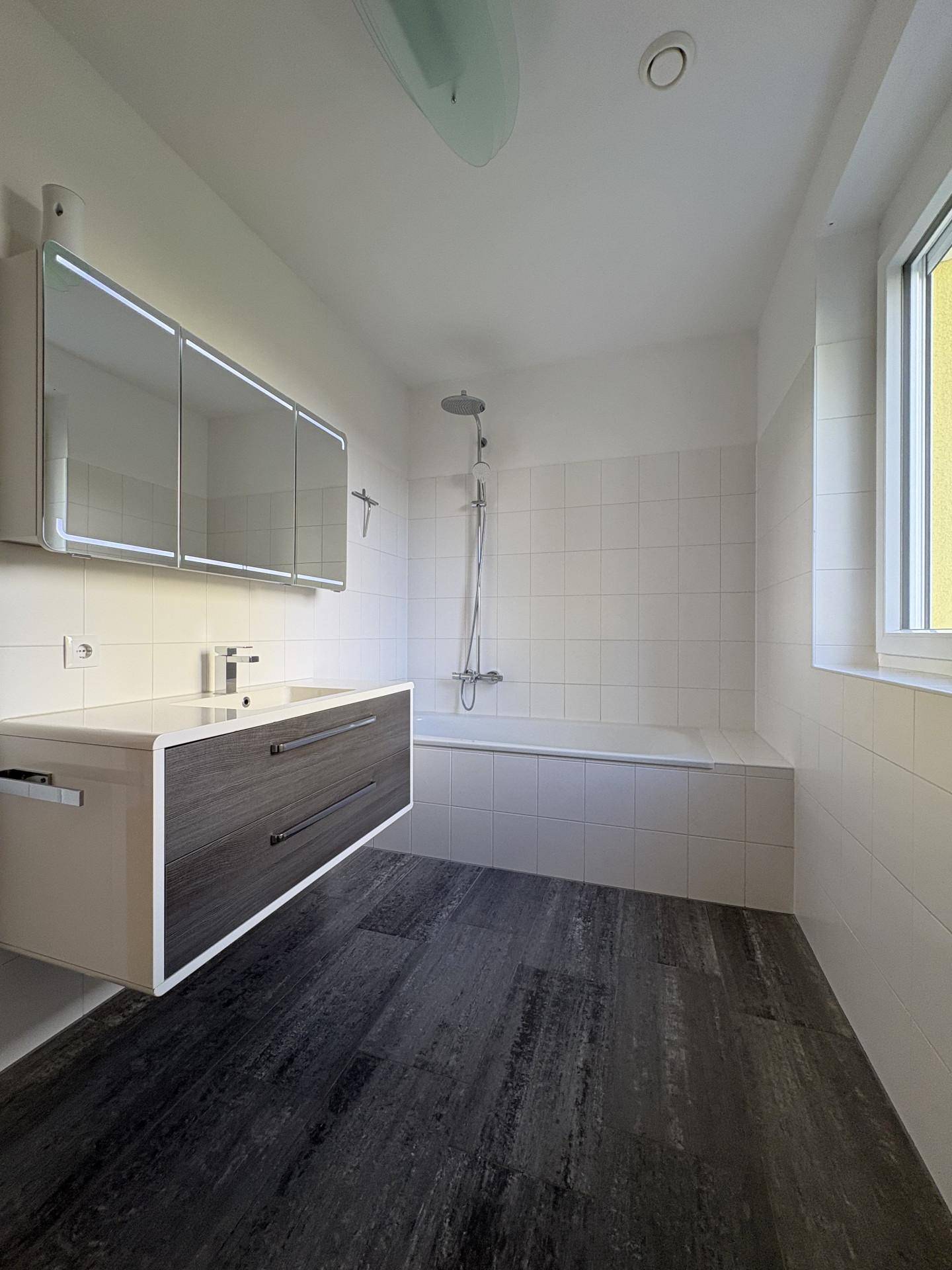 Modernes Badezimmer mit dunklen Fliesen, Badewanne und schwebendem Waschtisch mit Spiegelschrank.