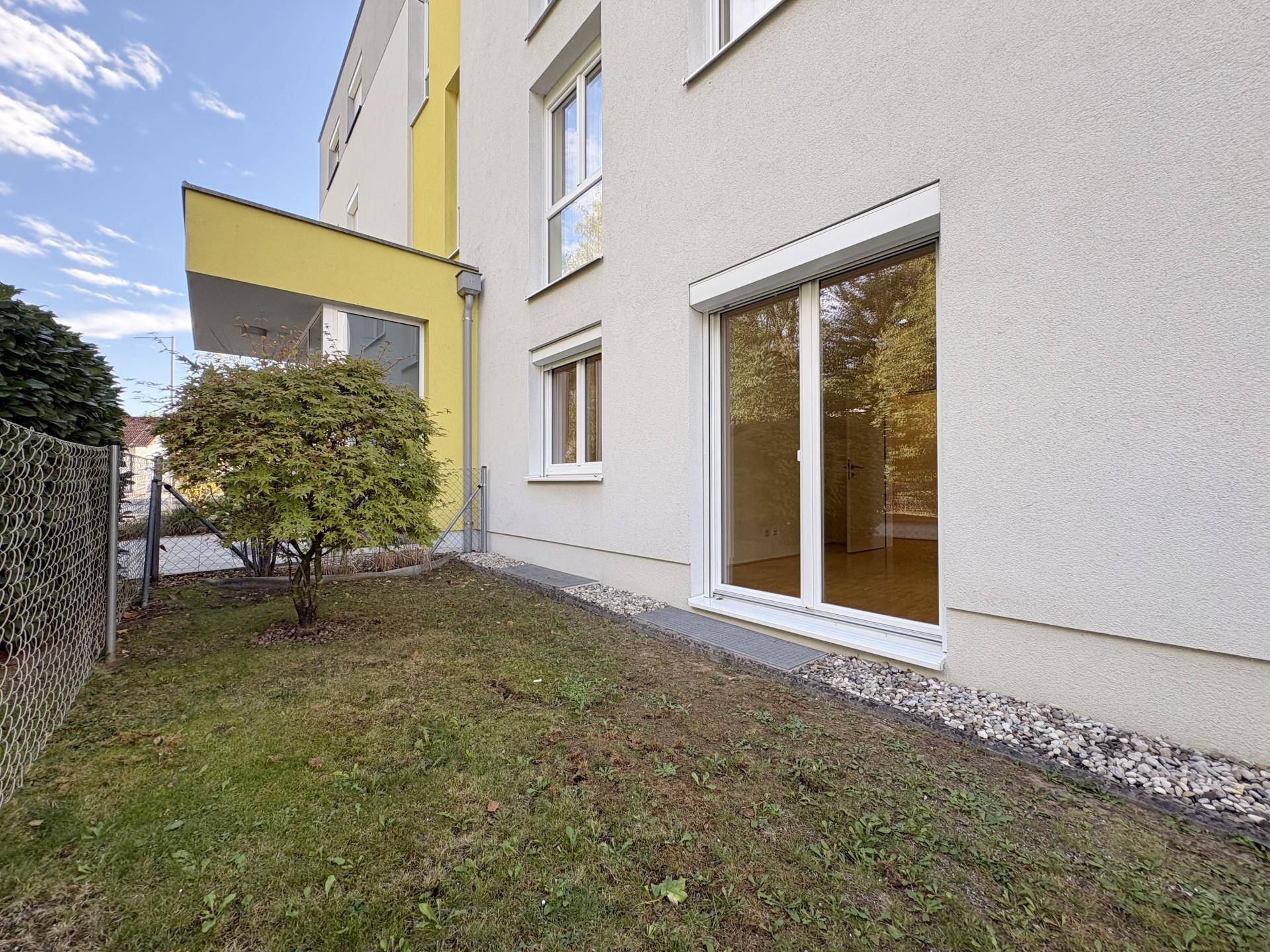 Seitenansicht des Gebäudes mit Rasenfläche und großem Fenster, das den Innenraum erhellt.