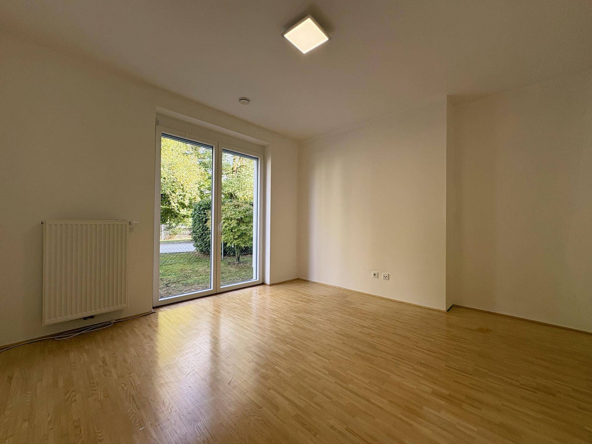 Geräumiges Zimmer mit Holzboden und direktem Zugang zum Garten, ideal als Schlaf- oder Arbeitszimmer.