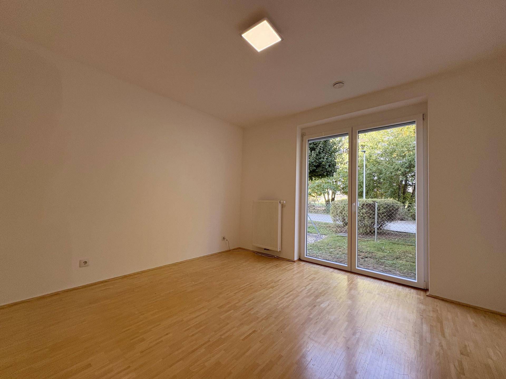 Helles Zimmer mit Holzboden und großen Fenstern, die viel Tageslicht hereinlassen und Zugang zum Außenbereich bieten.