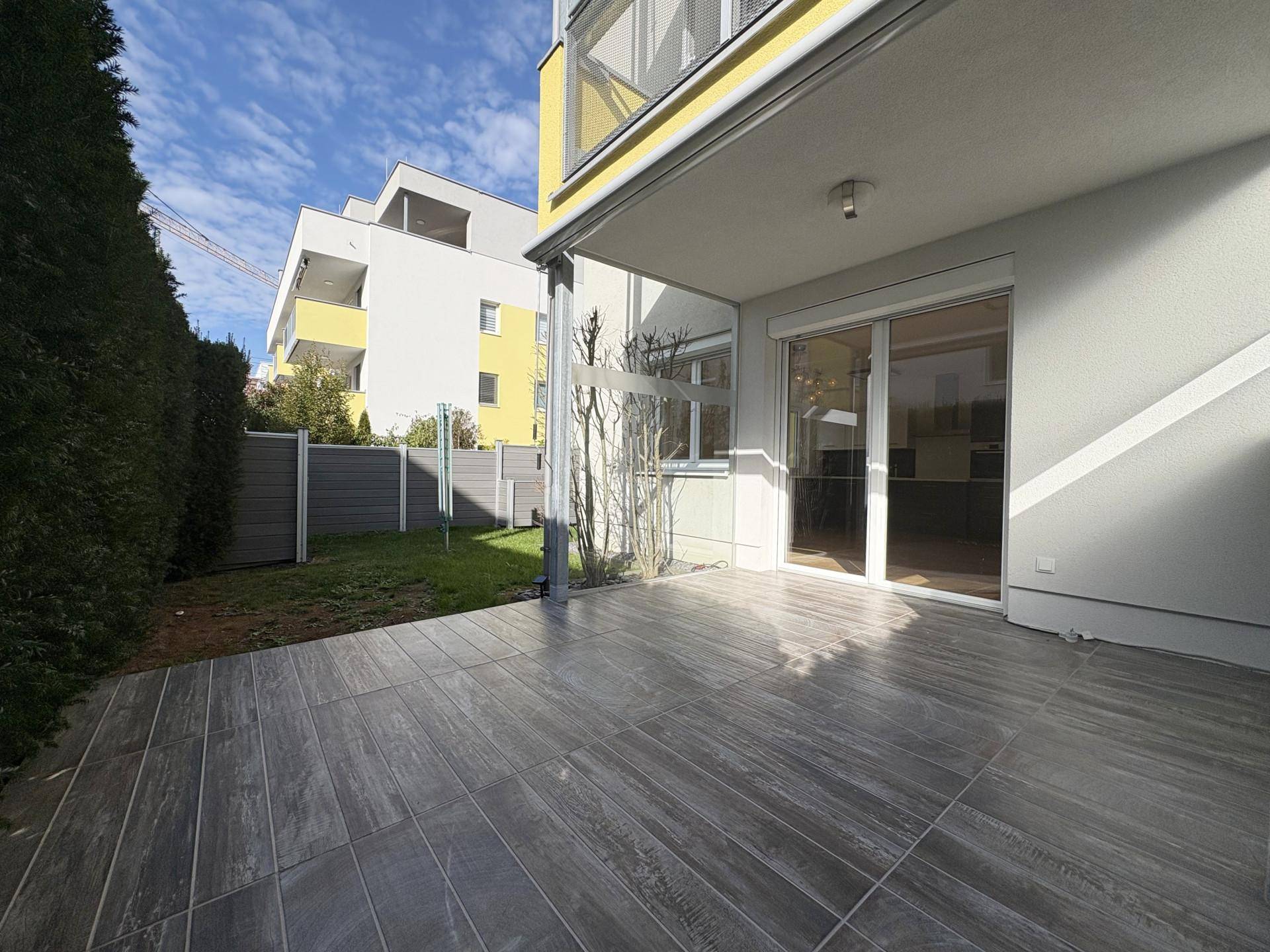 Sonnige Terrasse mit modernen Fliesen und angrenzendem Rasenbereich, ideal für entspannte Stunden im Freien.