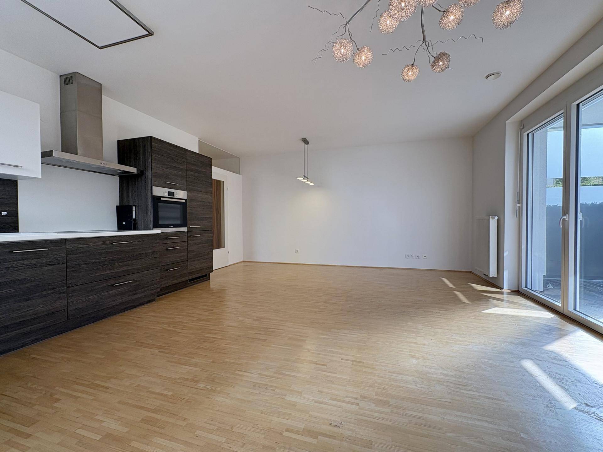Offener Wohnbereich mit integrierter Küche, Holzboden und viel Tageslicht durch große Fenster.