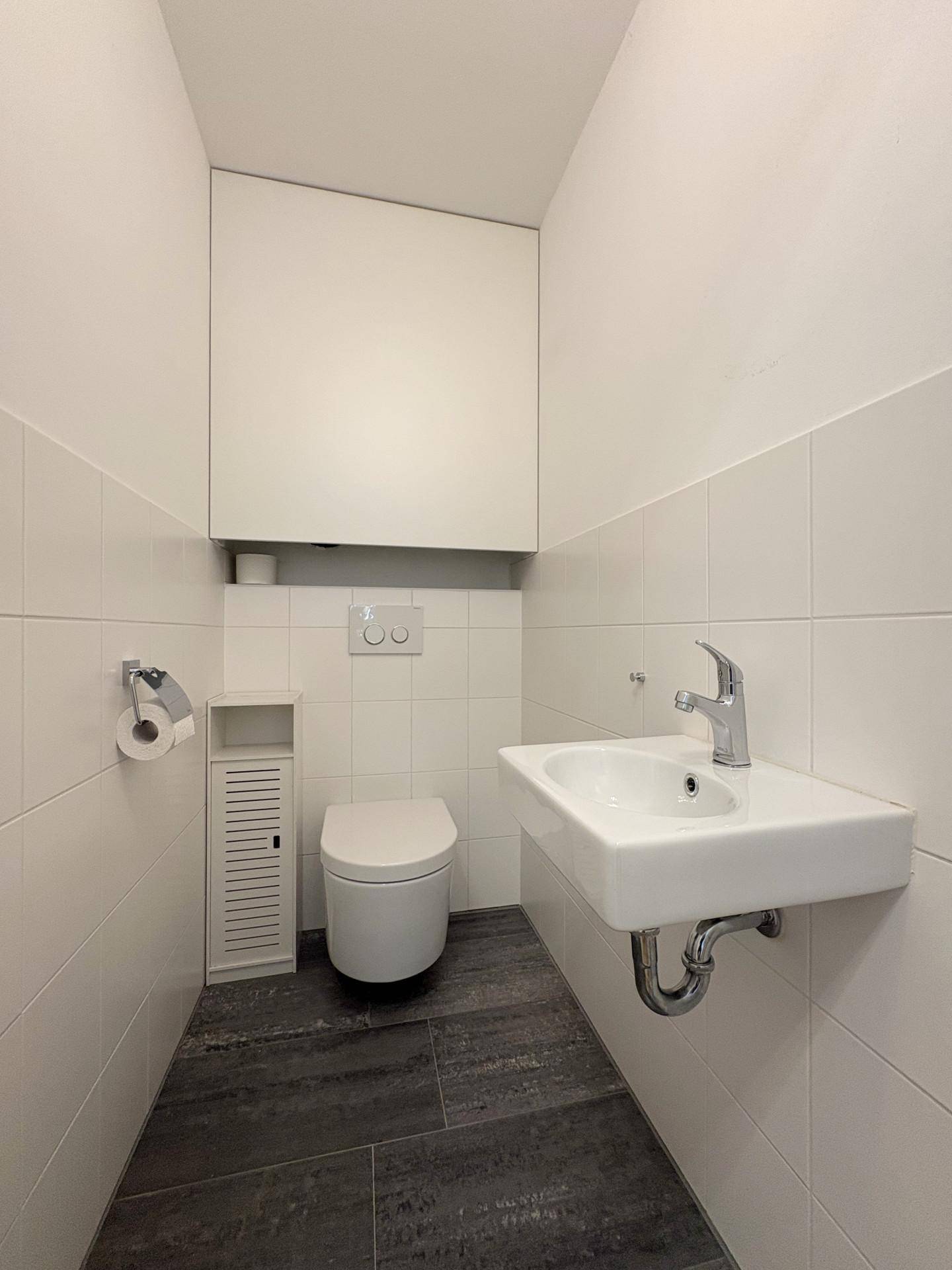 Funktionelles Gäste-WC mit modernen Fliesen, wandhängendem WC und kleinem Handwaschbecken.