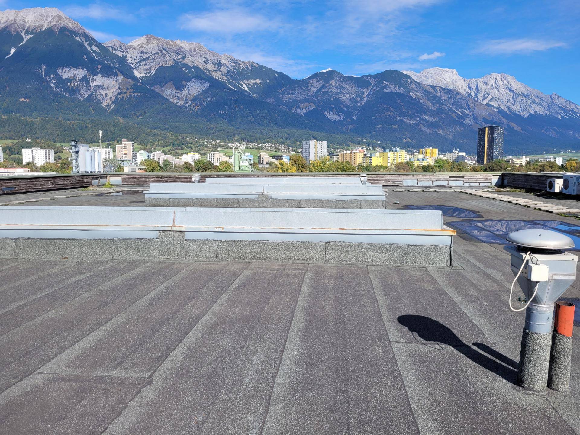 Flachdach eines Gebäudes mit weitem Blick auf die Stadt und die umliegenden Berge unter blauem Himmel.