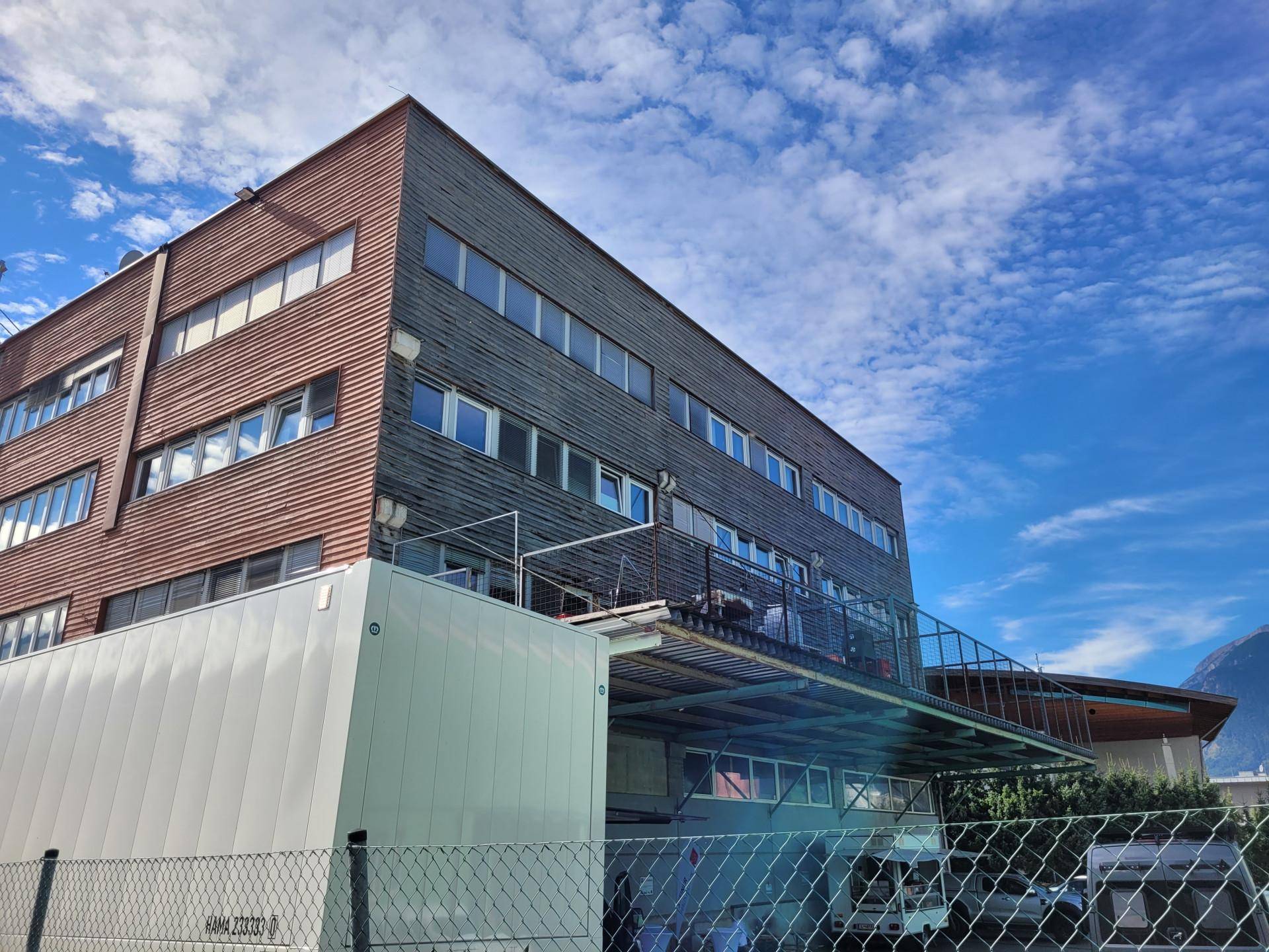Rückseite eines Geschäftsgebäudes mit Holzfassade und einer externen Metallkonstruktion unter bewölktem Himmel.