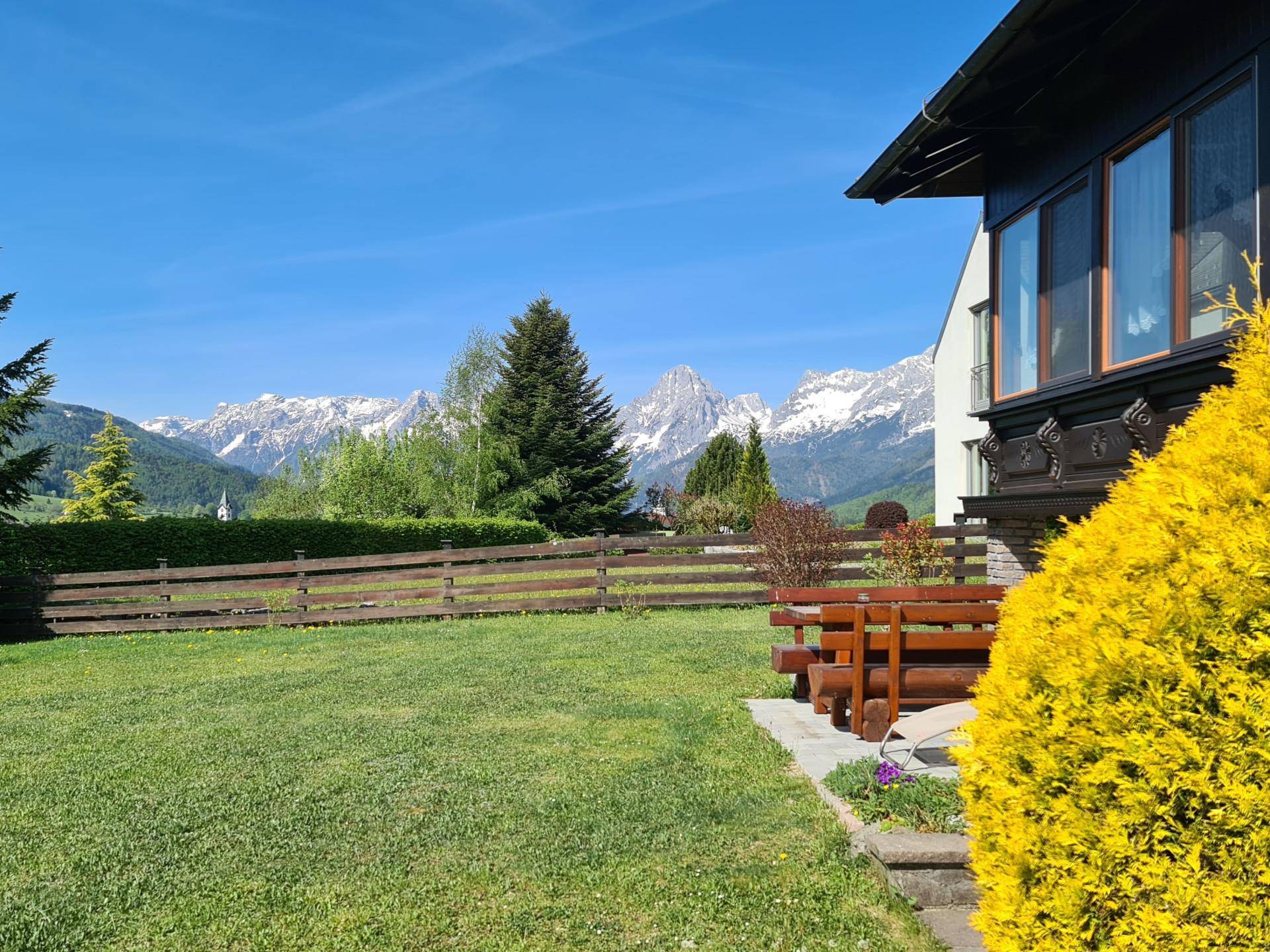 Weitläufiger Garten mit Bergblick und kleiner Sitzecke unter strahlend blauem Himmel.