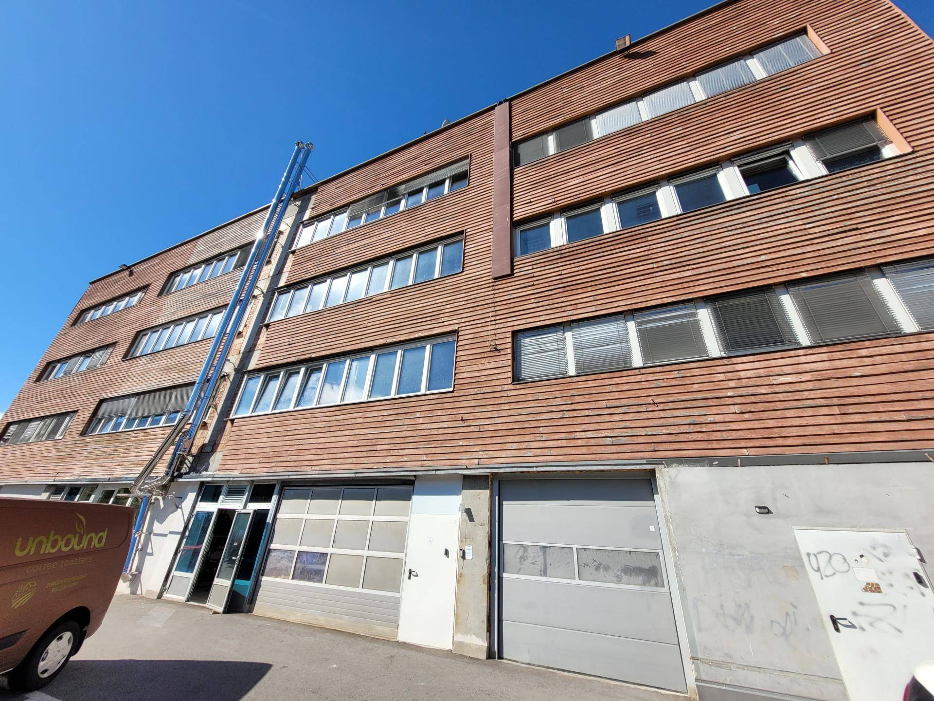 Seitenansicht eines Geschäftsgebäudes mit Holzfassade, Laderampe und Garagentoren im Erdgeschoss.