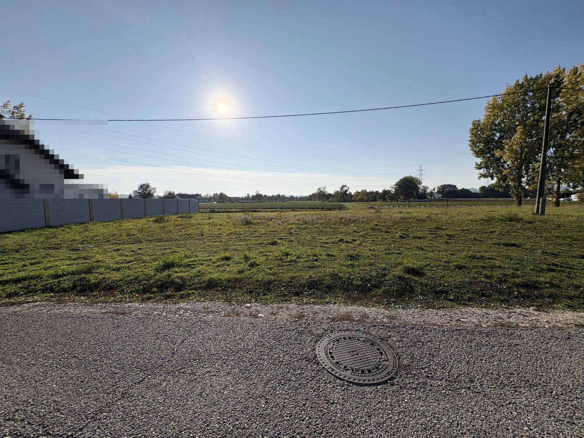 Sonniges Baugrundstück mit weitem Blick ins Grüne und Kanaldeckel im Vordergrund.
