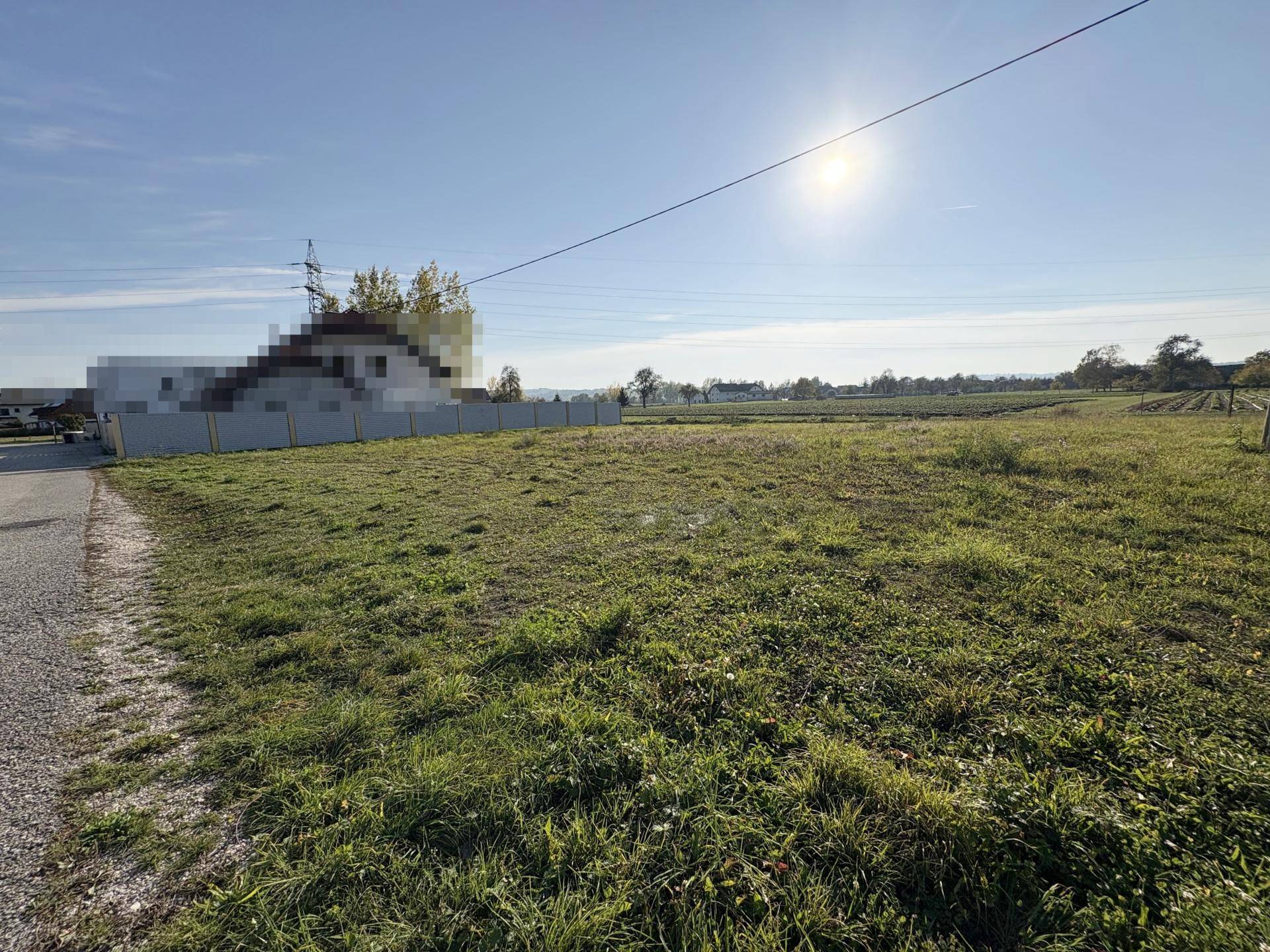 Offenes Grundstück mit Grasfläche und sonnigem Himmel, umgeben von ländlicher Umgebung.