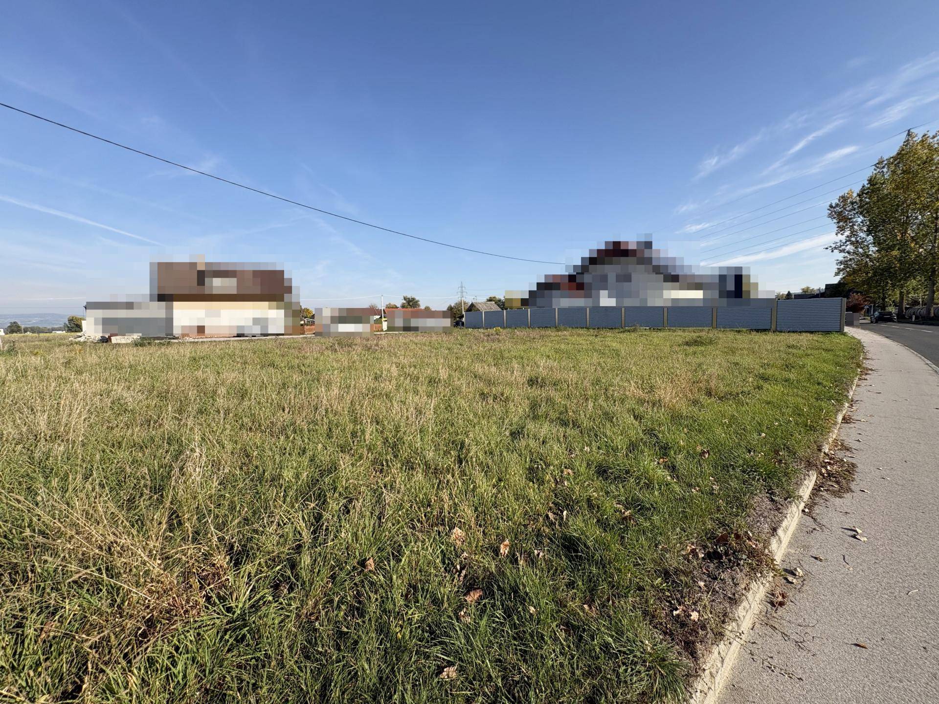 Weitläufiges Baugrundstück mit angrenzender Straße und Blick auf umliegende Häuser.