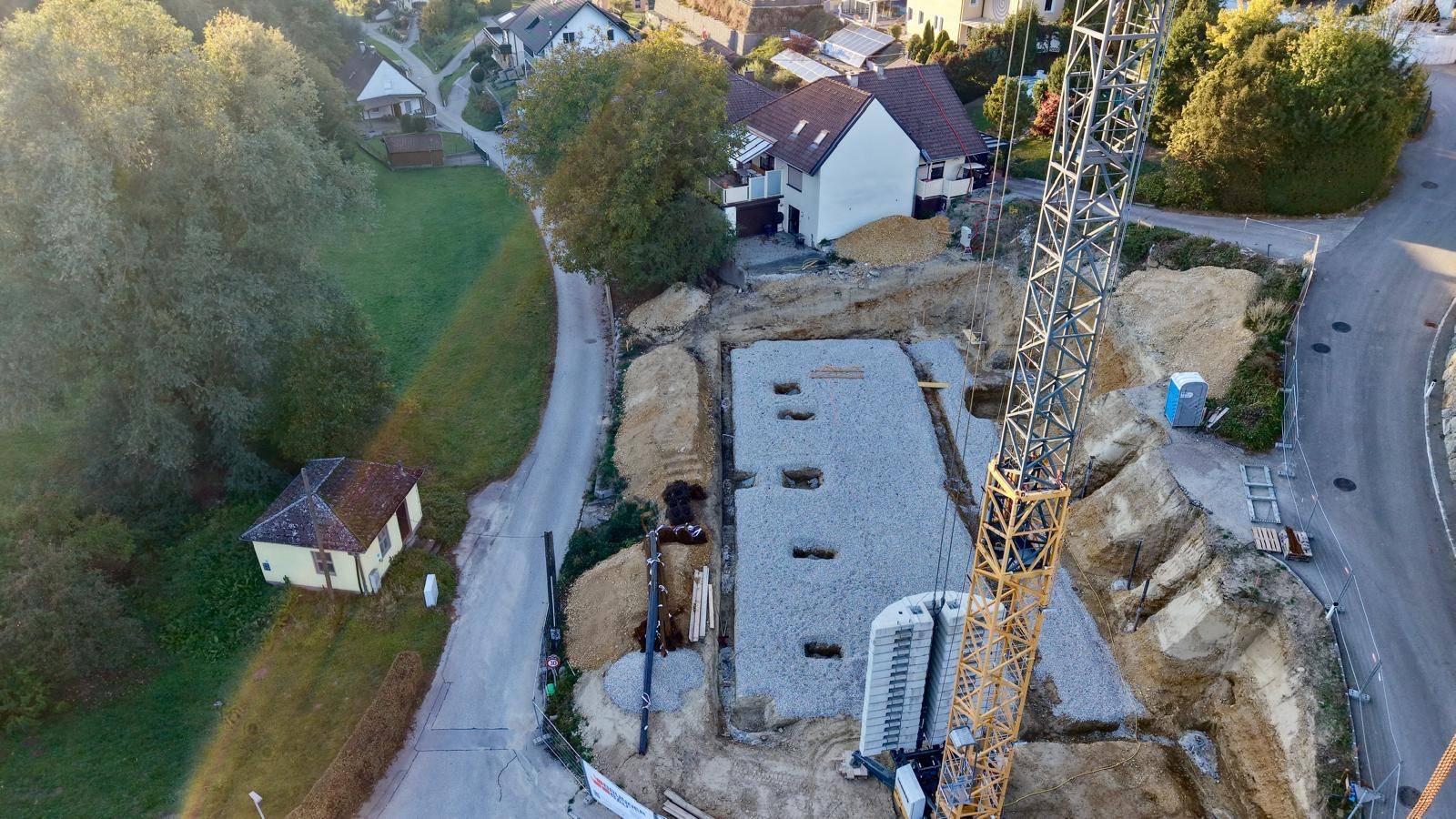 Nahaufnahme einer Baustelle mit Fundamentarbeiten und einem Kran in ländlicher Umgebung.
