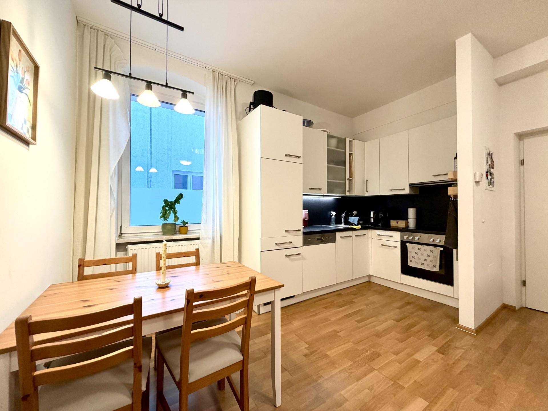 Helle Wohnküche mit weißer Einbauküche, Holztisch und Parkettboden.