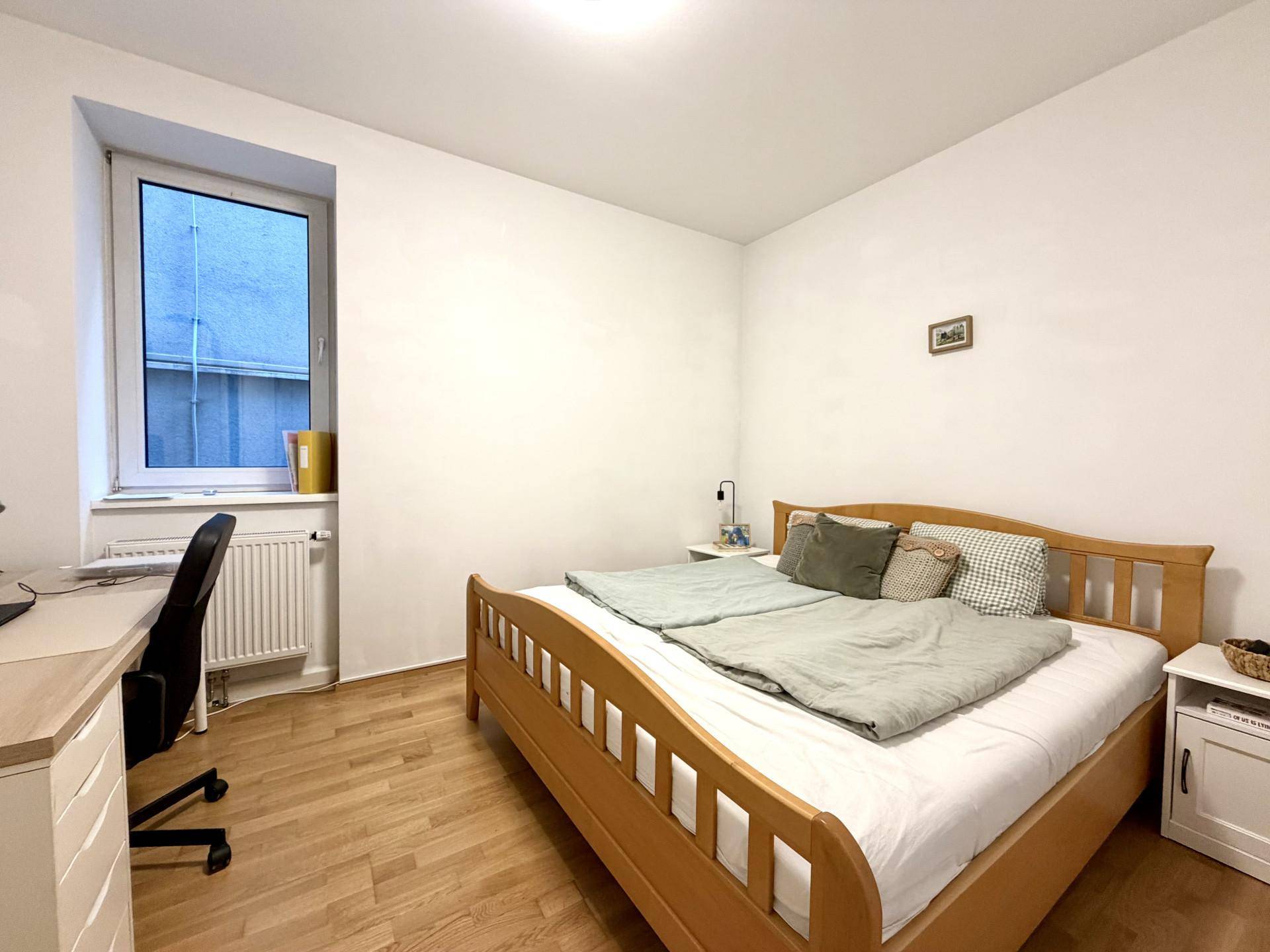 Helles Schlafzimmer mit Holzbett, Schreibtisch und Parkettboden.
