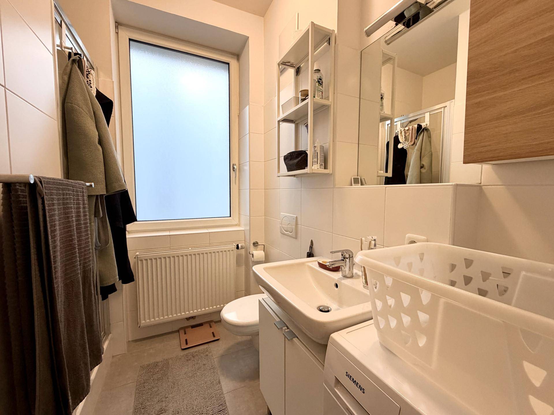 Modernes Badezimmer mit Fenster, Waschbecken, Toilette und Fliesenboden.