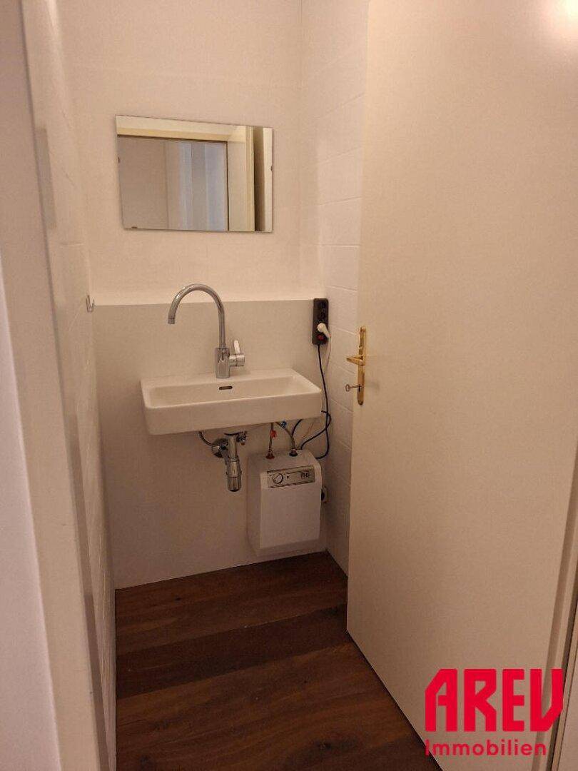 Kleines Gäste-WC mit modernem Waschbecken, Spiegel und Holzboden.