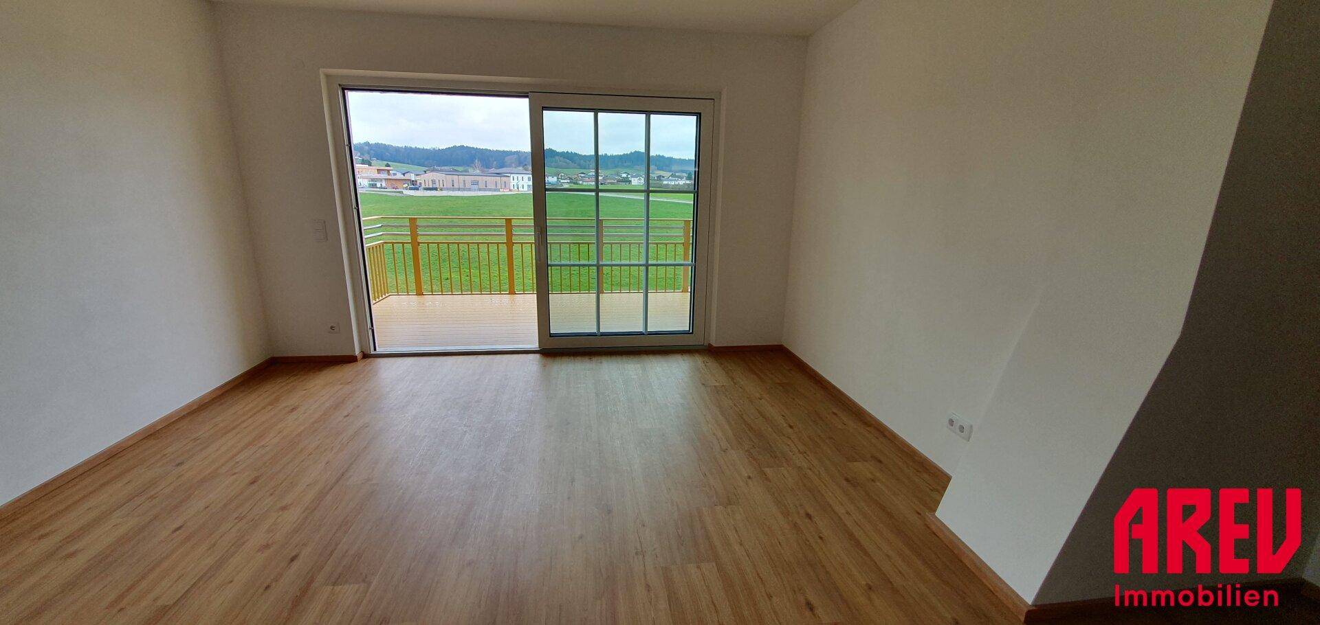 Leerer Raum mit Holzboden und großen Schiebetüren, die zu einem Balkon führen.