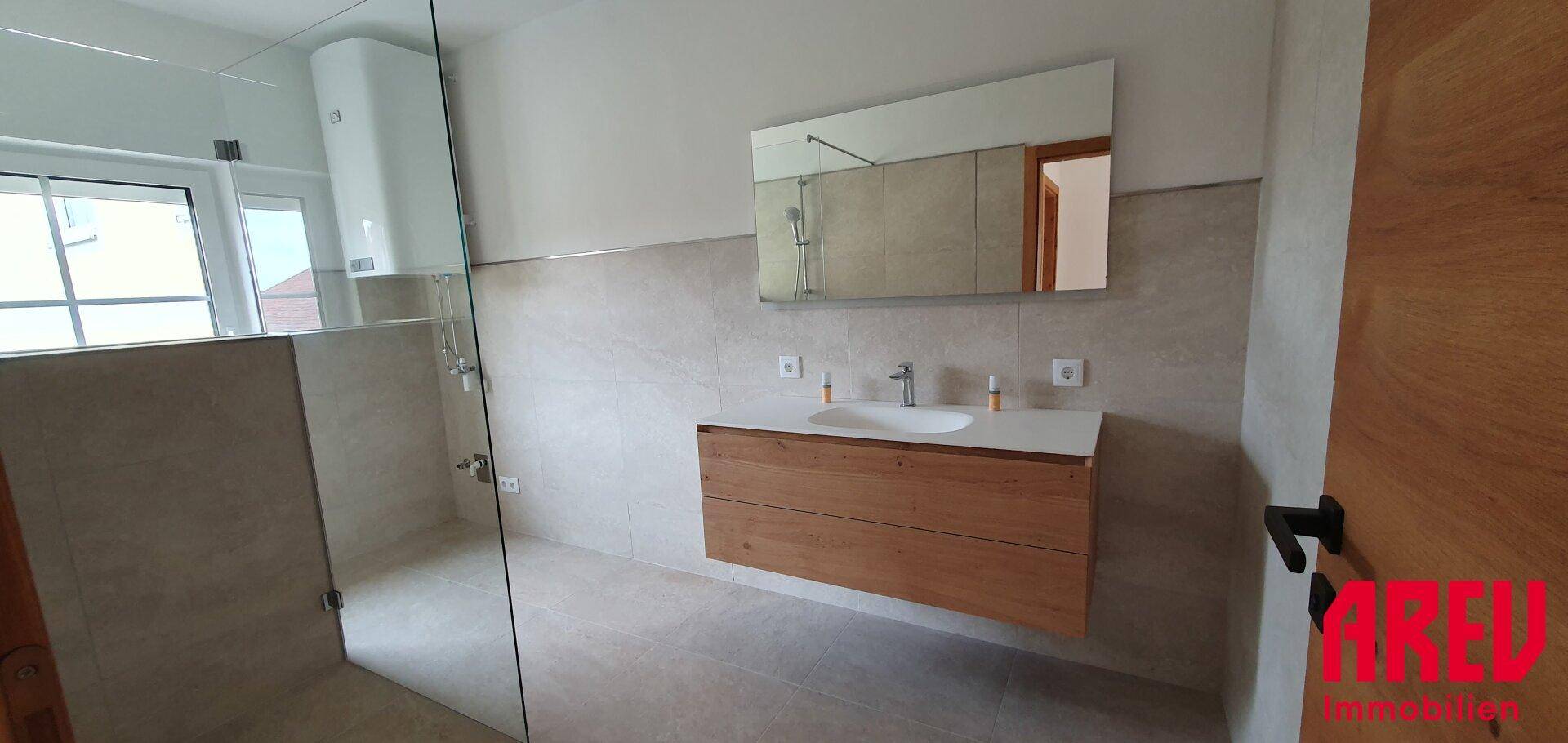 Modernes Badezimmer mit begehbarer Dusche, Holzwaschtisch und großem Spiegel.