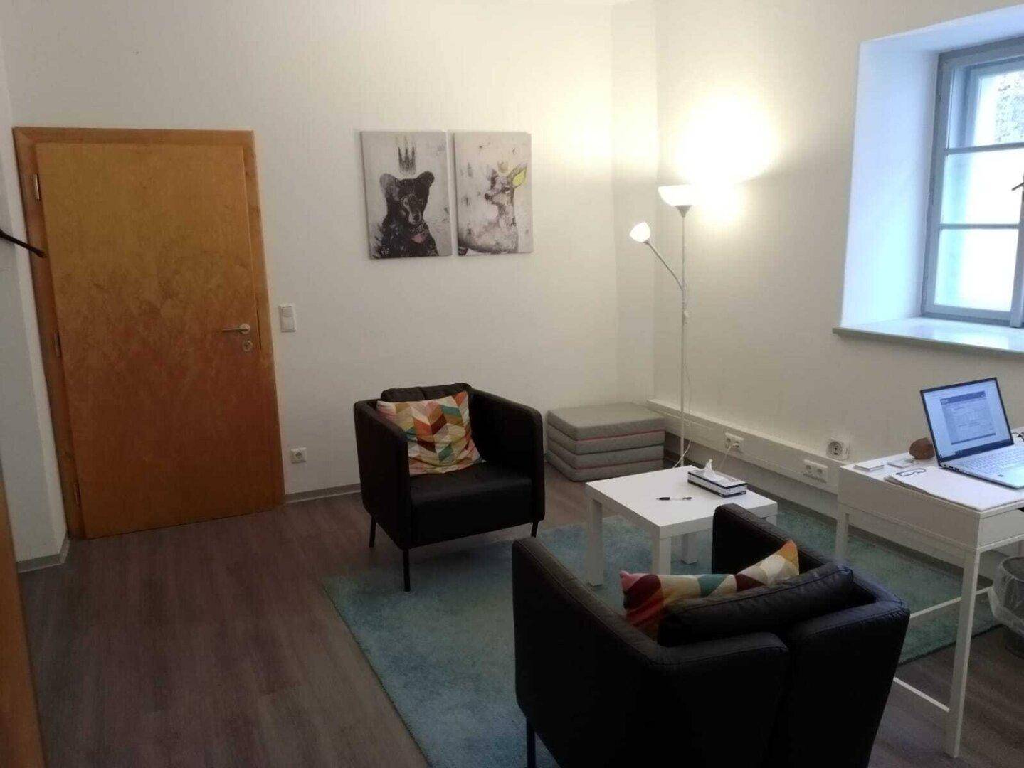 Helles Büro mit zwei schwarzen Sesseln, einem Schreibtisch und einem Fenster mit natürlichem Licht.