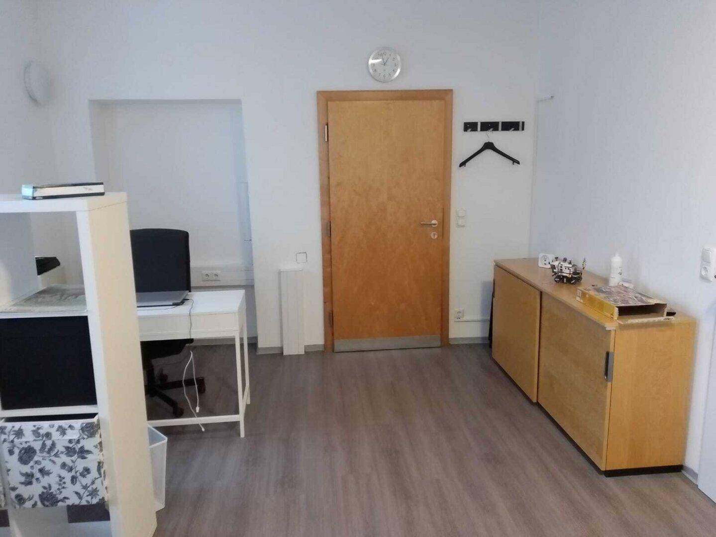 Empfangsbereich mit einem weißen Schreibtisch, Holzschränken und einer Holztür in einem hellen Raum.