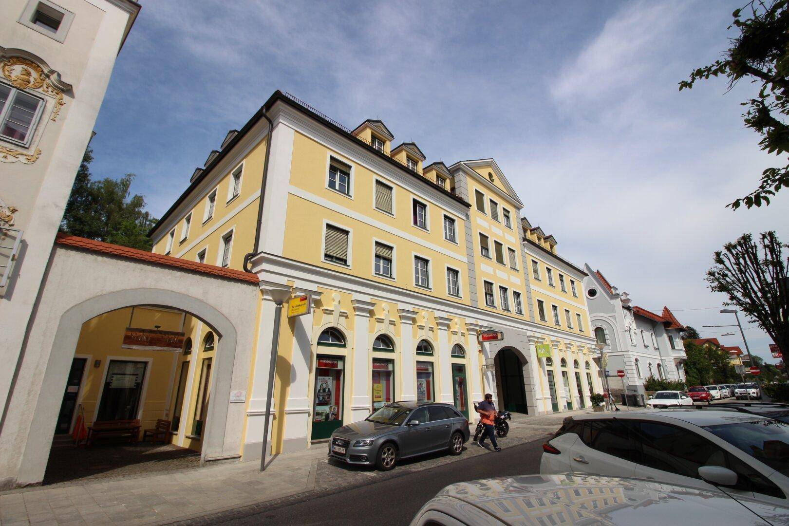 Seitenansicht des gelben Gebäudes mit klassischer Architektur, vielen Fenstern und Geschäften im Erdgeschoss.