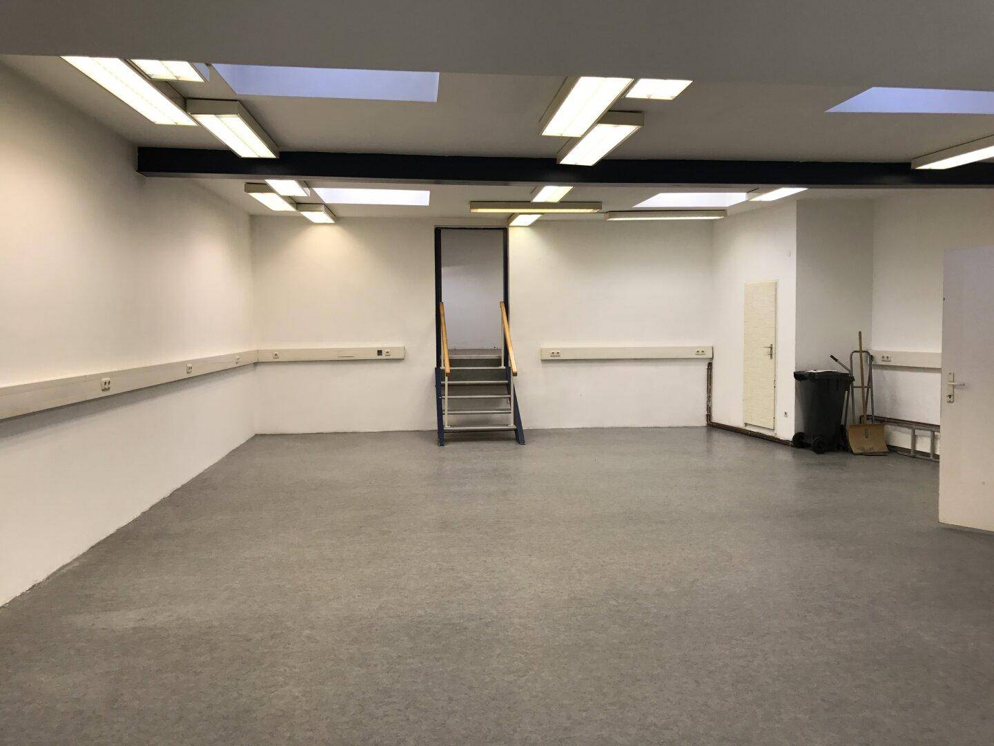 Großer, leerer Gewerberaum mit hohen Decken, Oberlichtern und funktionaler Beleuchtung, bereit zur individuellen Gestaltung.