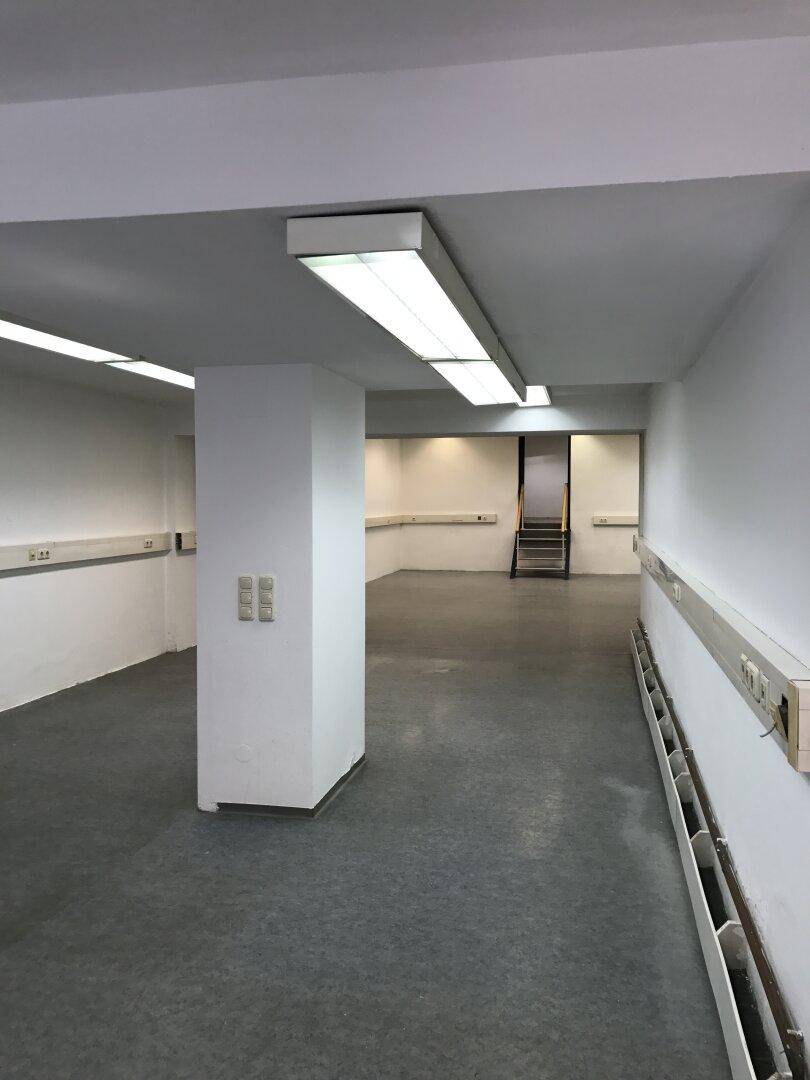 Geräumiger, leerer Gewerberaum mit Säule in der Mitte, grauen Böden und weißen Wänden, funktional beleuchtet.