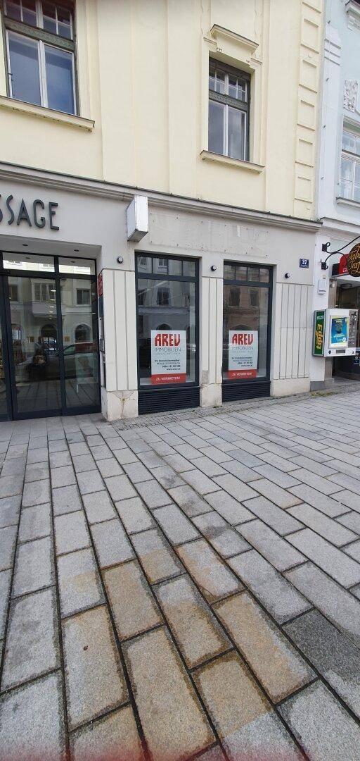 Gebäudefassade mit Schaufenstern und Pflastersteinen auf dem Bürgersteig, mit 'AREU' Werbeschildern.