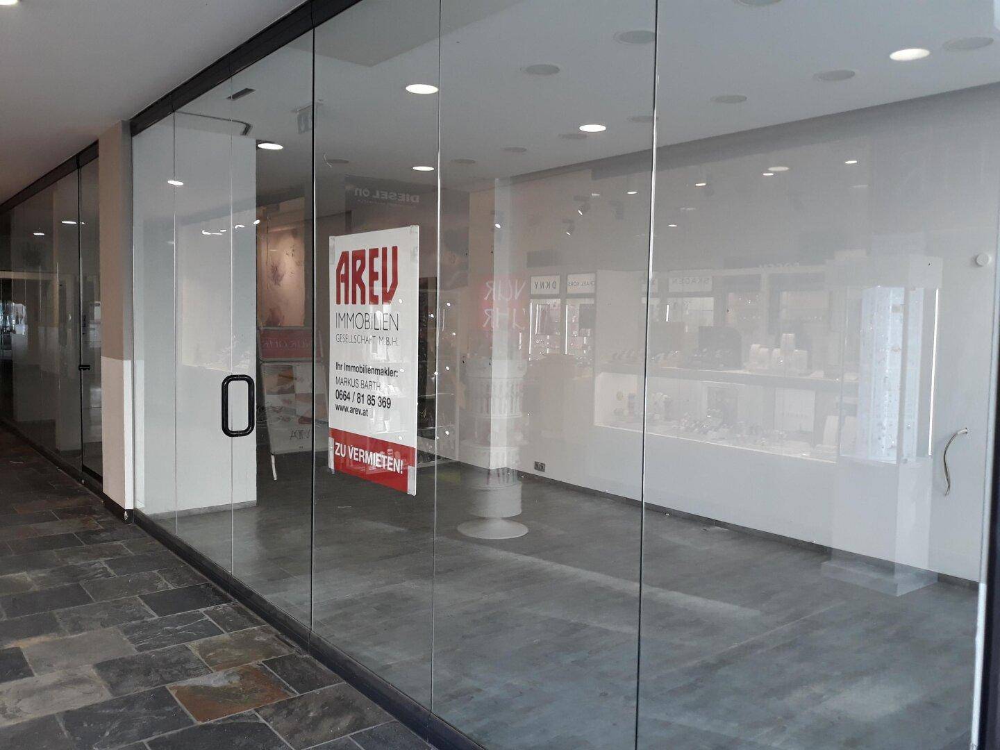 Leeres Ladengeschäft mit großen Glasfronten und einem 'AREU' Immobilienplakat an der Scheibe.