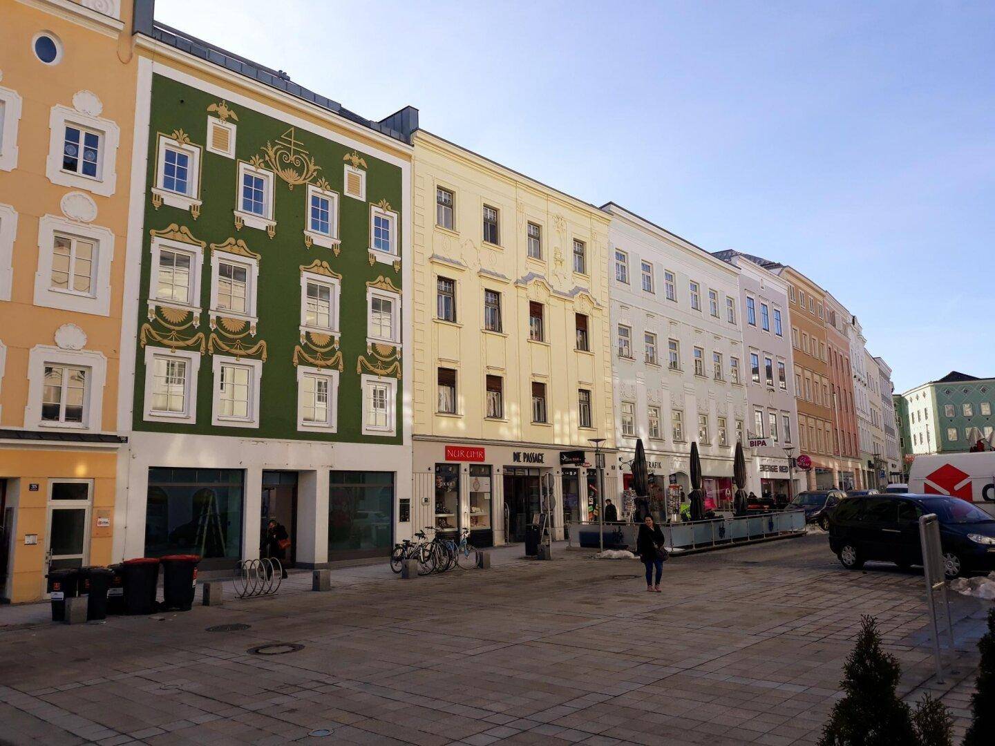 Historische Gebäudezeile mit farbigen Fassaden und Geschäften entlang einer belebten Straße in der Stadt.