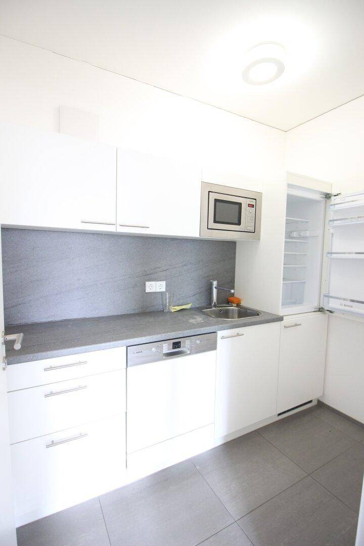 Moderne Küchenzeile mit weißen Schränken, integrierten Geräten und Fliesenboden, praktisch und funktional.