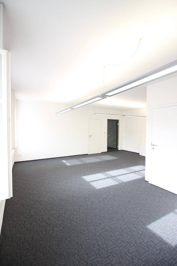 Geräumiger Bürobereich mit Teppichboden, hellen Wänden und effizienter Deckenbeleuchtung, bietet vielseitige Nutzungsmöglichkeiten.