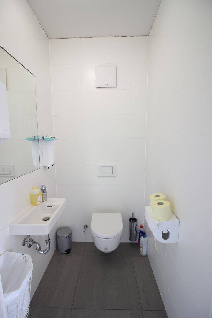 Kleines, hell gefliestes WC mit wandhängender Toilette und Waschbecken, sauber und funktional gestaltet.