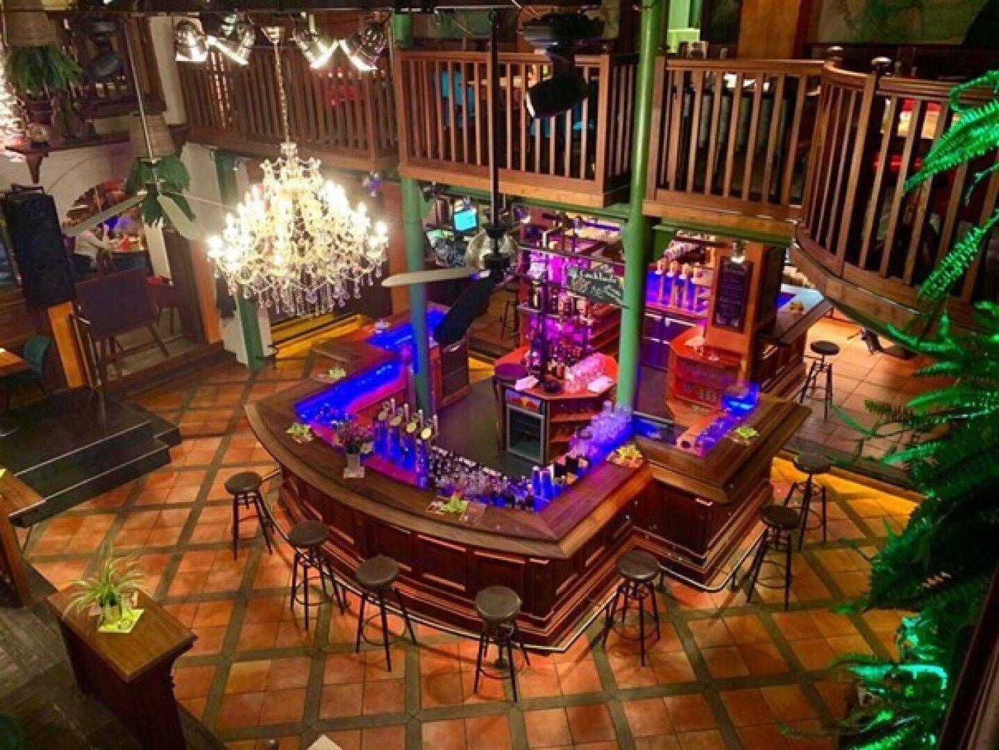 Bar-Bereich mit leuchtender Theke, Hockern und einer Galerie im Obergeschoss, beleuchtet von einem Kronleuchter.
