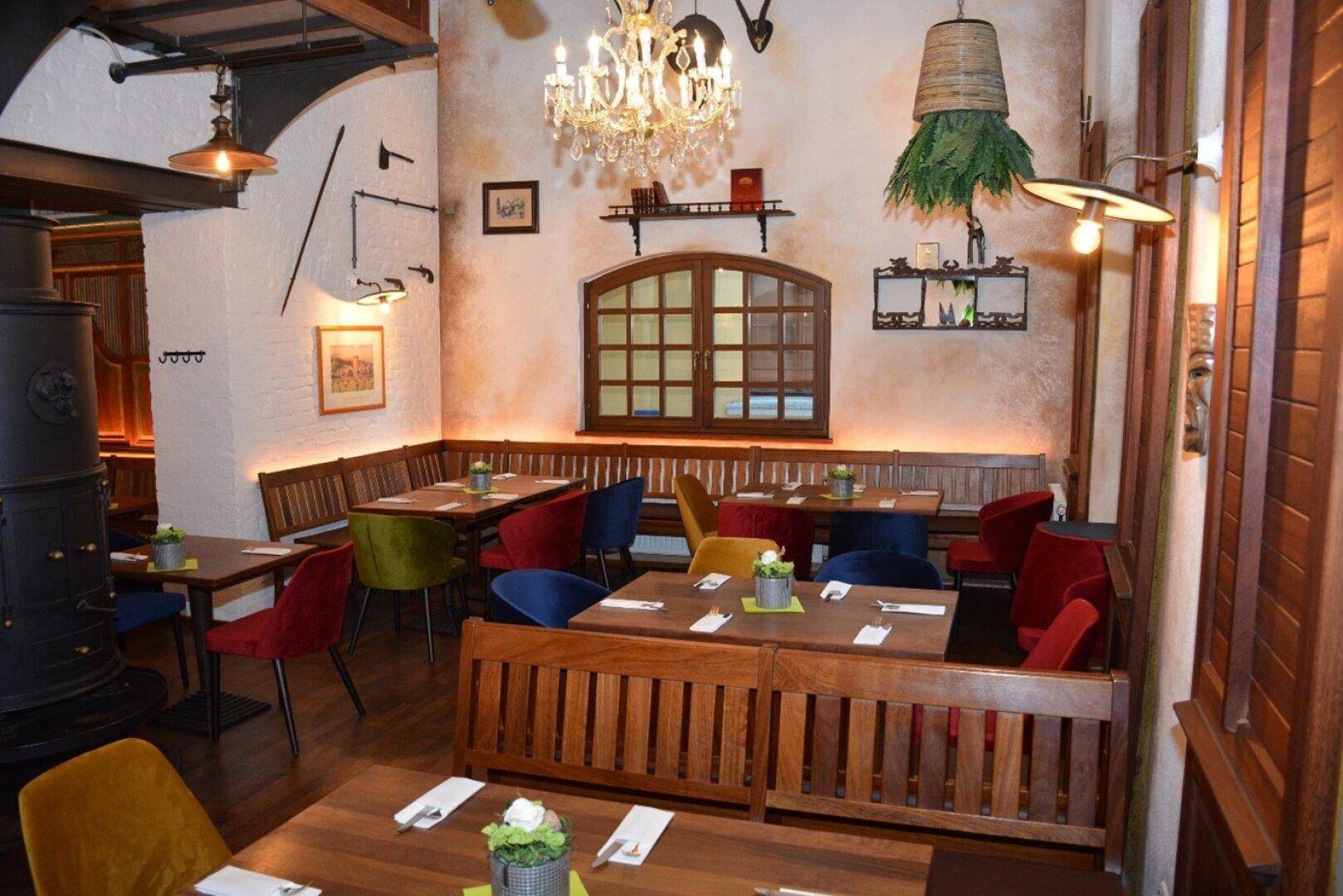 Gemütlicher Restaurantbereich mit Holzbänken, bunten Stühlen, Holztischen und einem traditionellen Kaminofen.