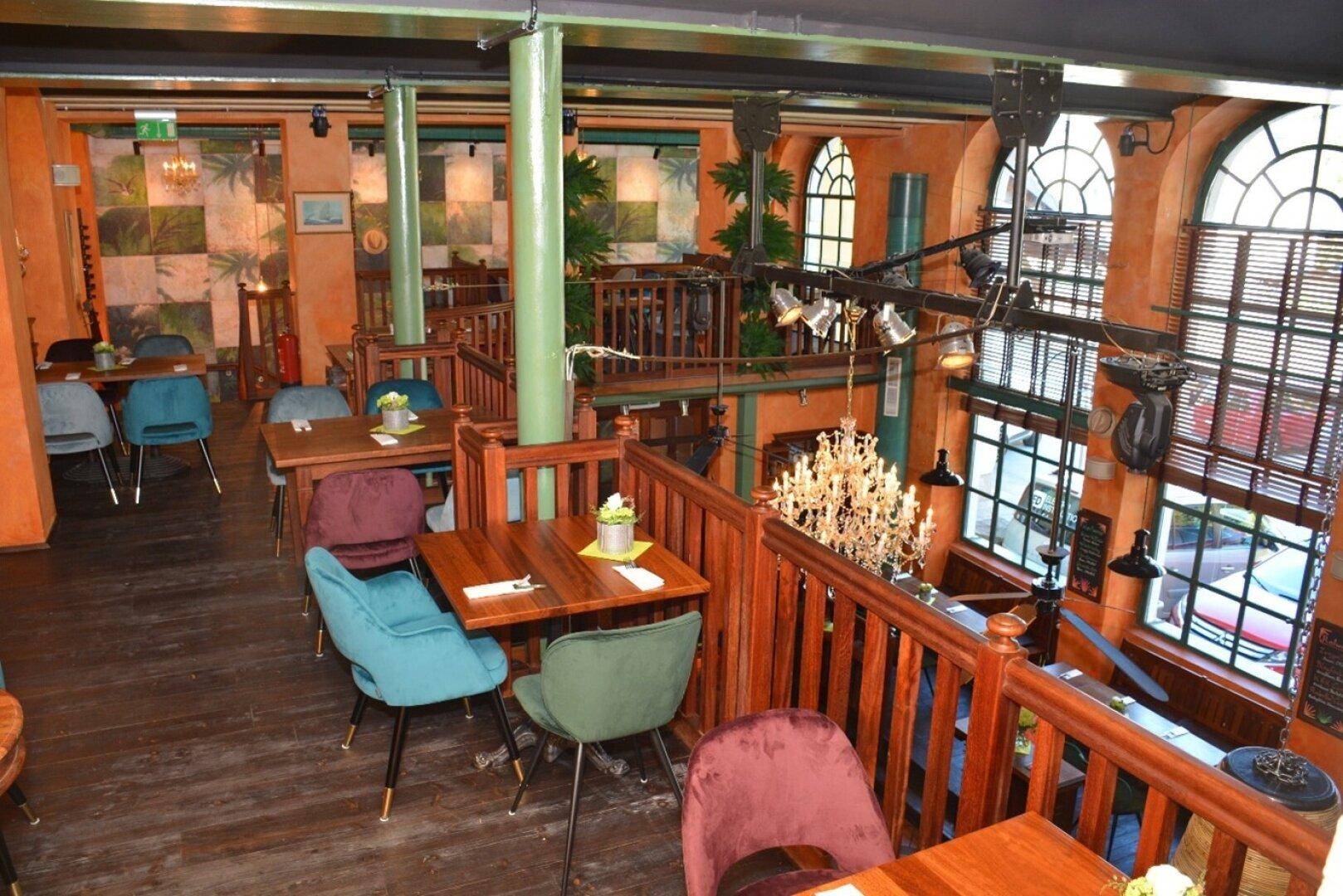 Restaurantbereich mit Blick auf die obere Galerie, Holztischen und großen Bogenfenstern, die viel Licht hereinlassen.