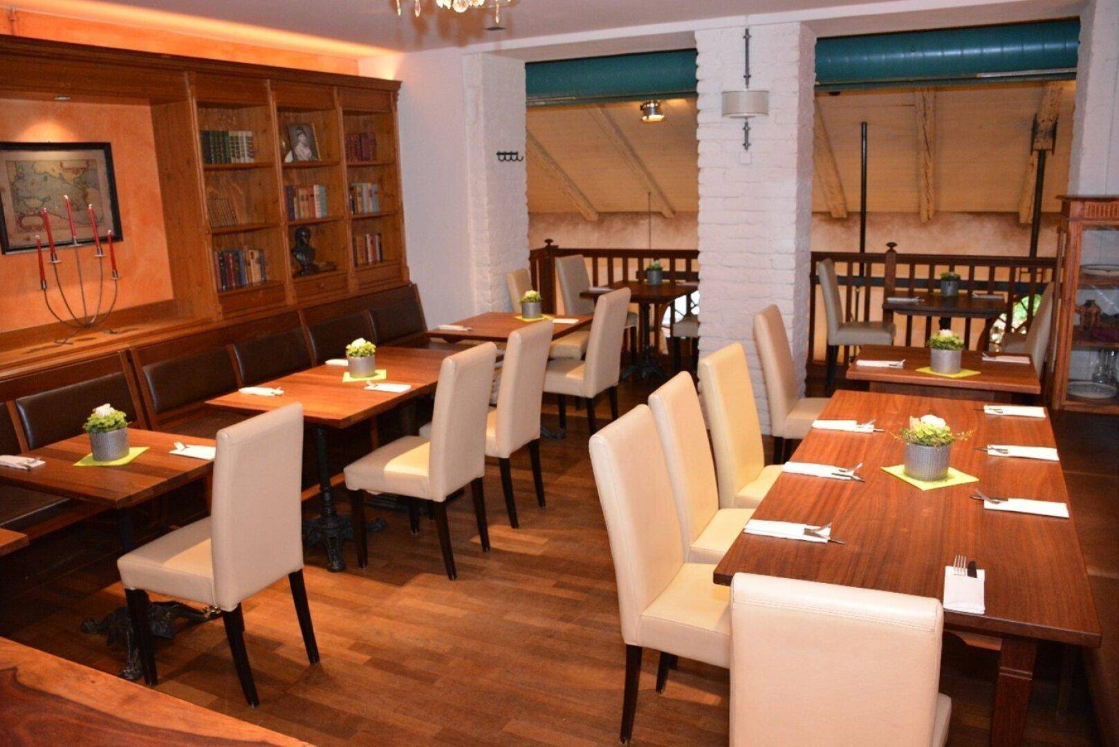 Gemütlicher Restaurantbereich mit Holzbänken, einem Bücherregal und hellen Stühlen an Holztischen.