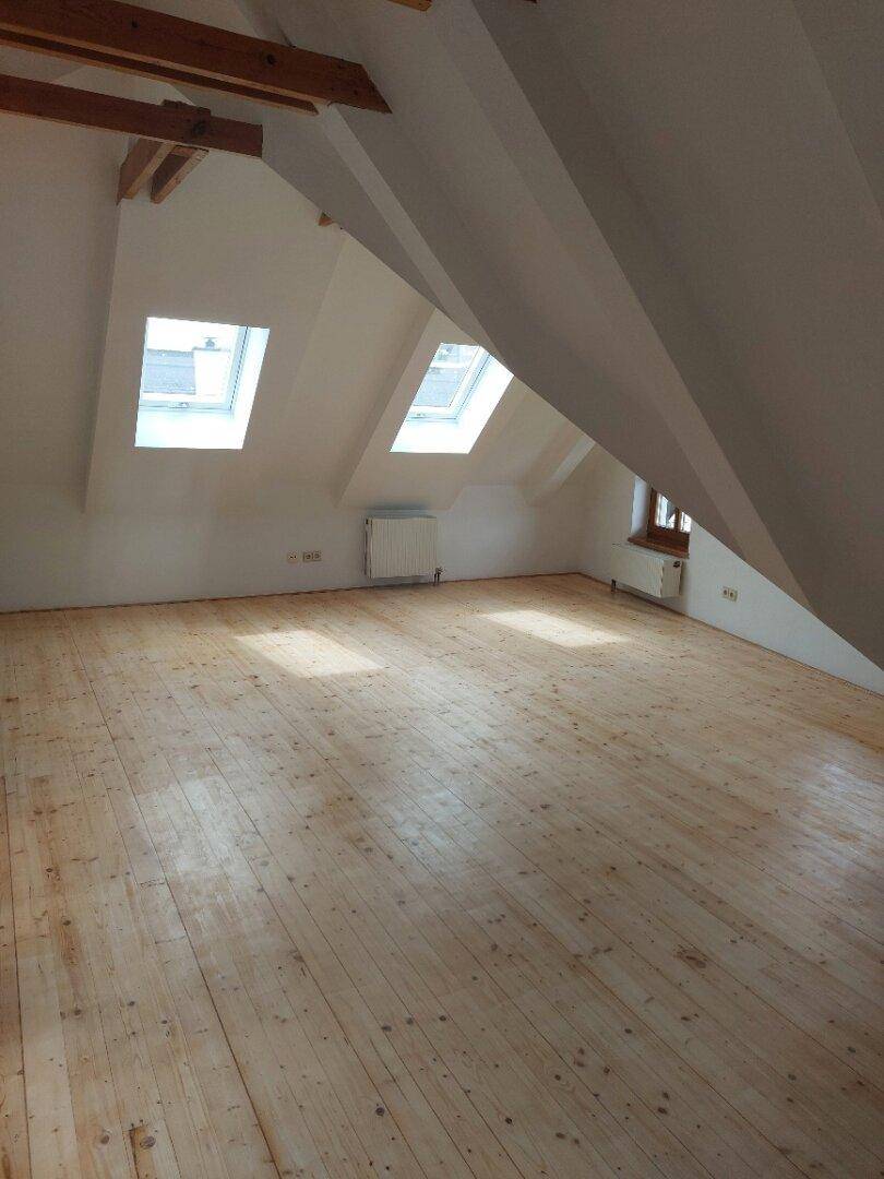 Geräumiges Dachzimmer mit Holzdielenboden, Dachfenstern und viel natürlichem Licht.