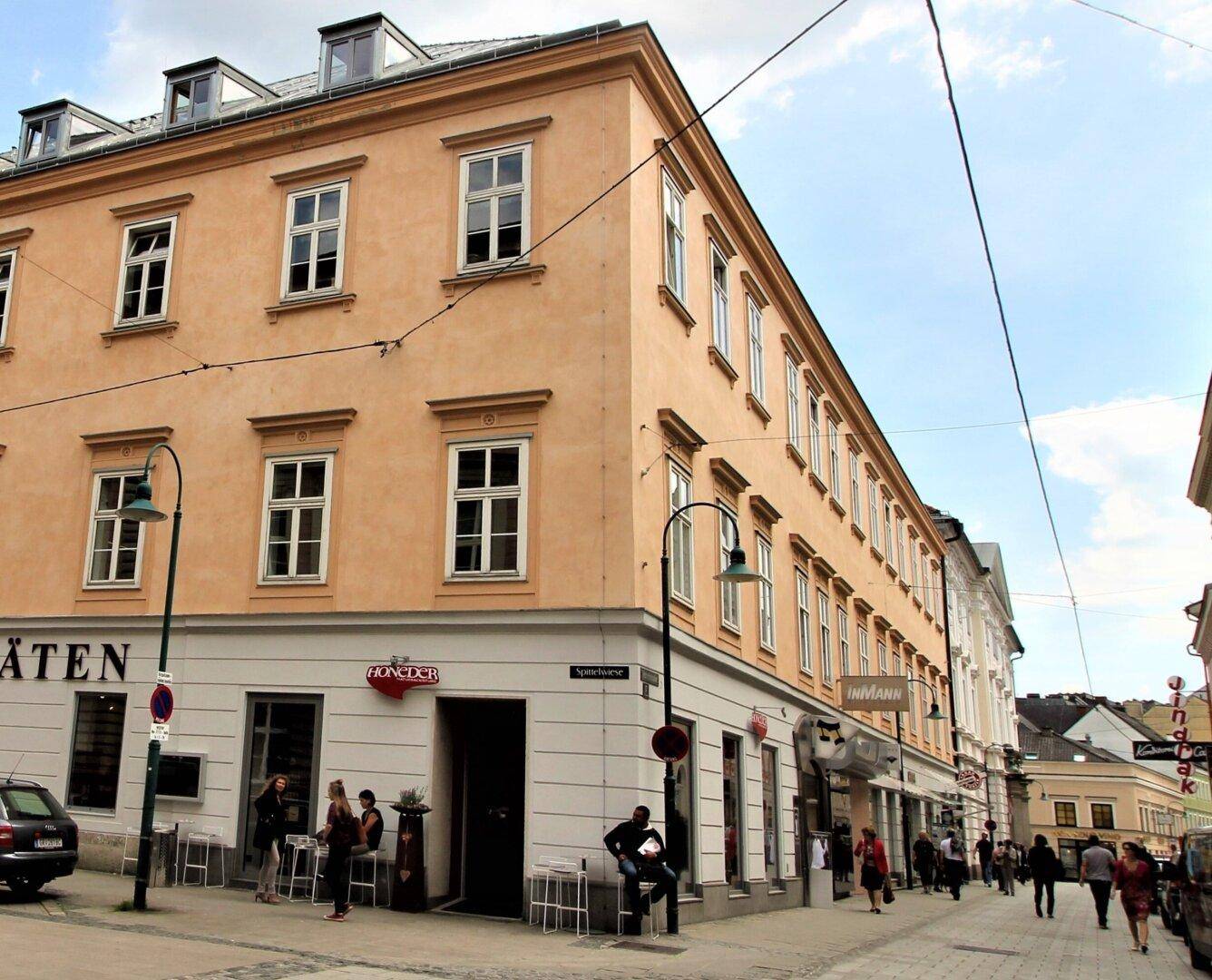 Historisches Gebäude an einer belebten Straße mit Geschäften und Passanten.