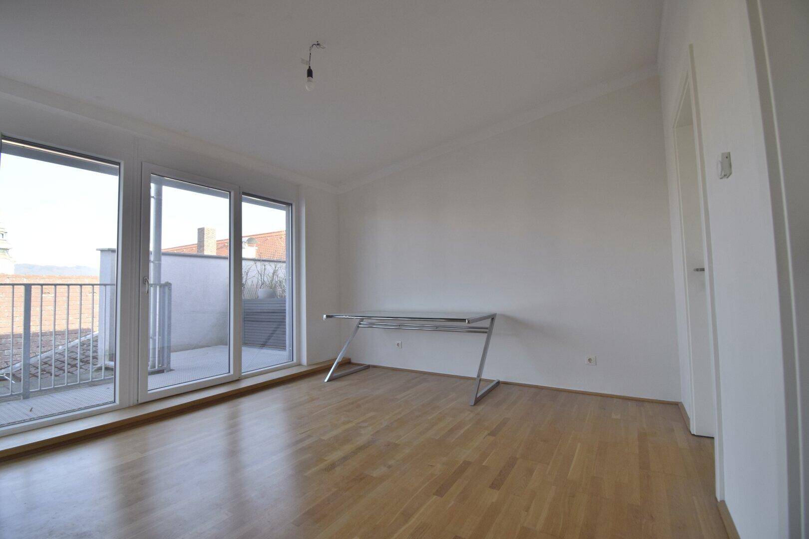Heller Raum mit Holzboden, großen Fenstern und Zugang zu einem Außenbereich.