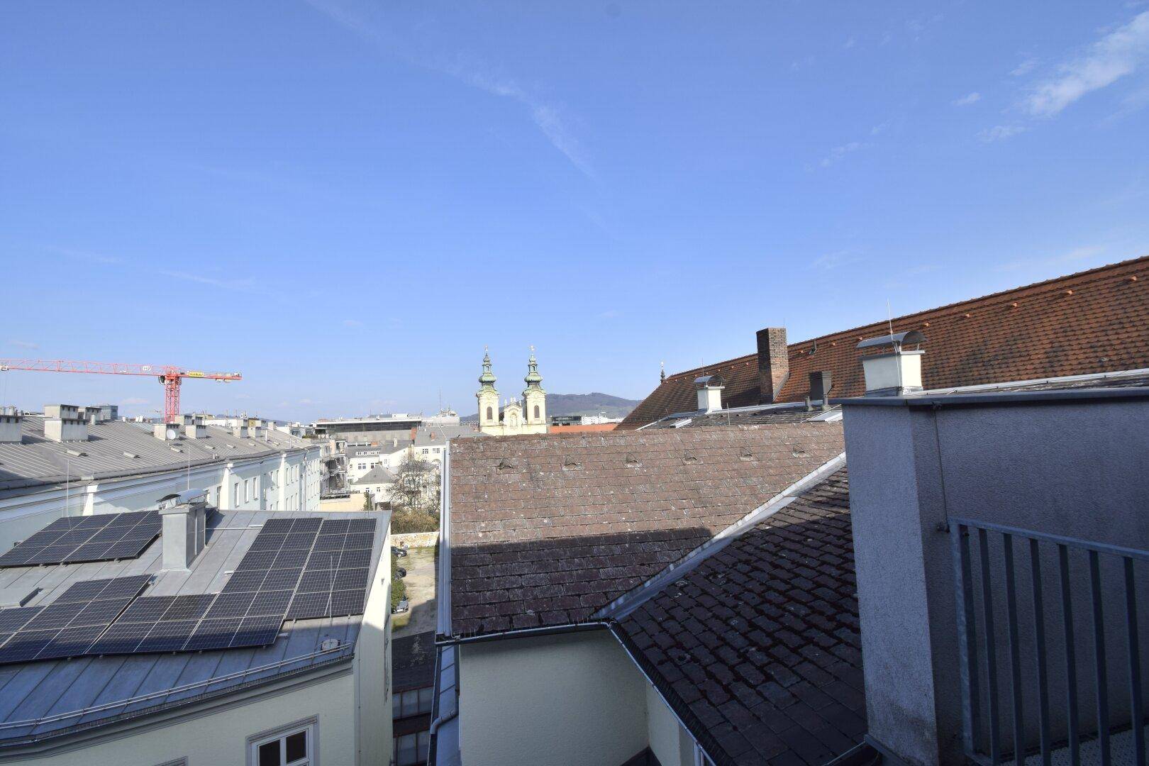 Weitläufiger Blick über Dächer der Stadt mit Kirchtürmen und Solaranlagen.