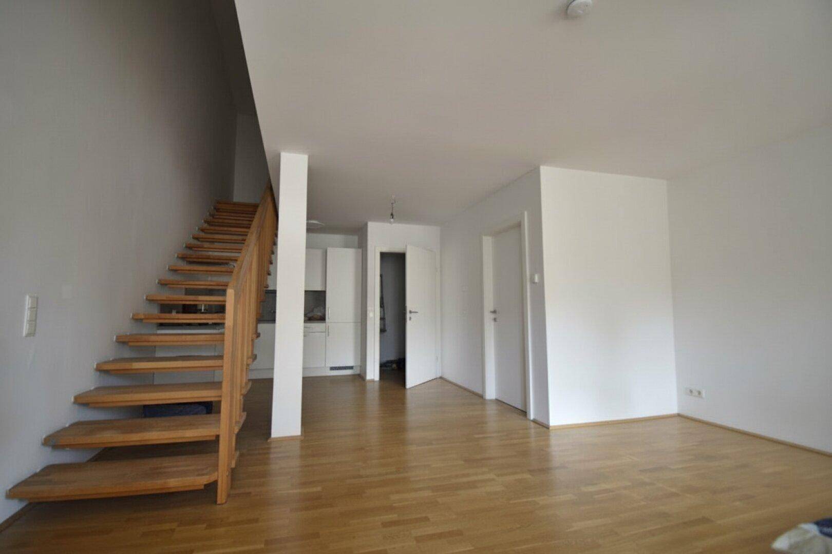 Offener Wohnbereich mit Holzboden und einer freistehenden Holztreppe.