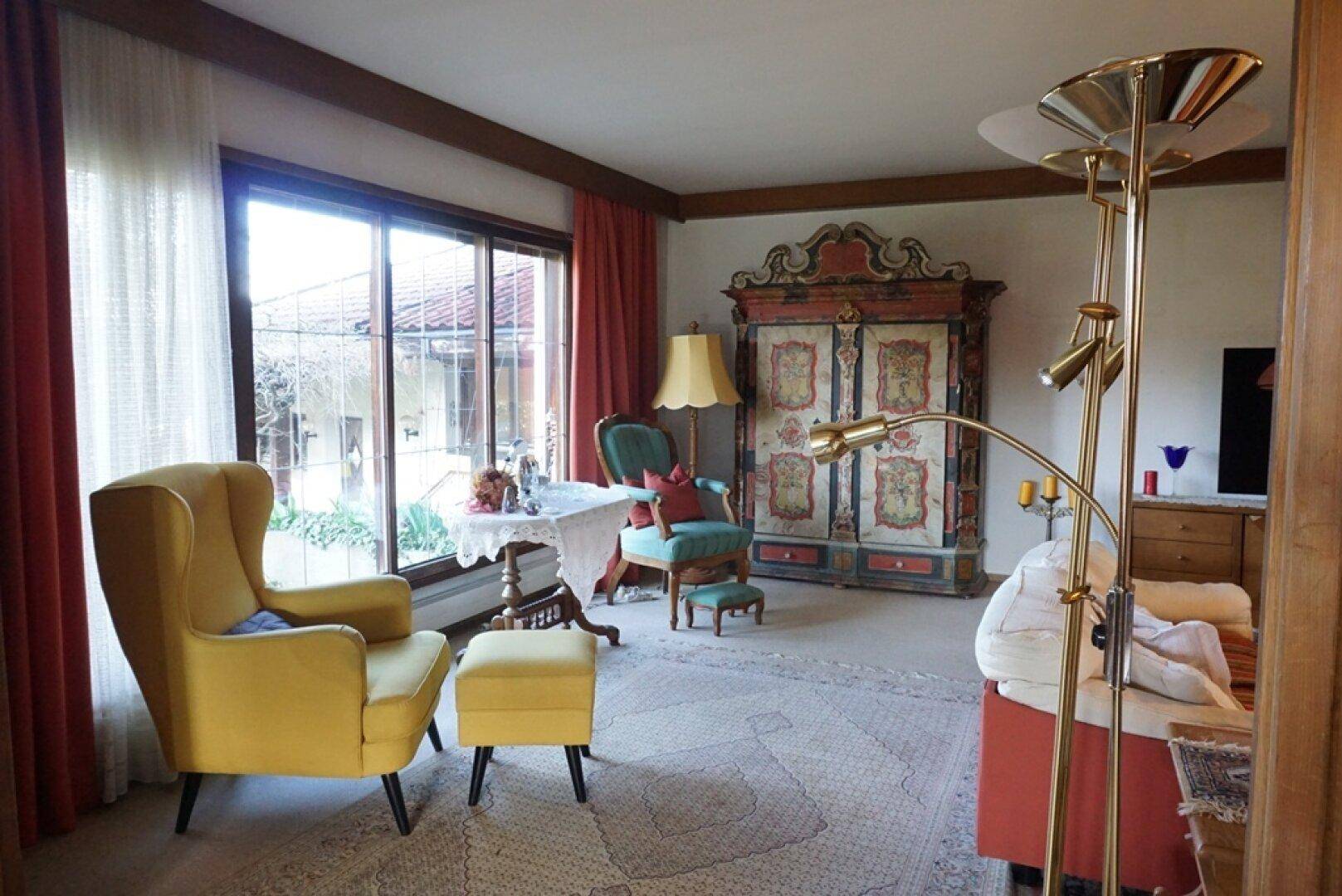 Helles Wohnzimmer mit großen Fenstern, traditionellen Möbeln und farbenfrohen Akzenten.