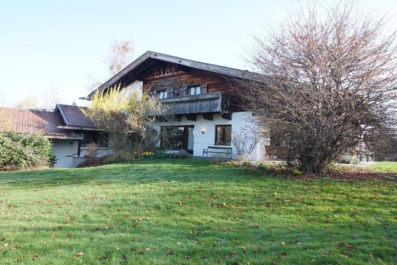 Traditionelles Haus mit weißer Fassade und Holzbalkon, umgeben von einem gepflegten Rasen.
