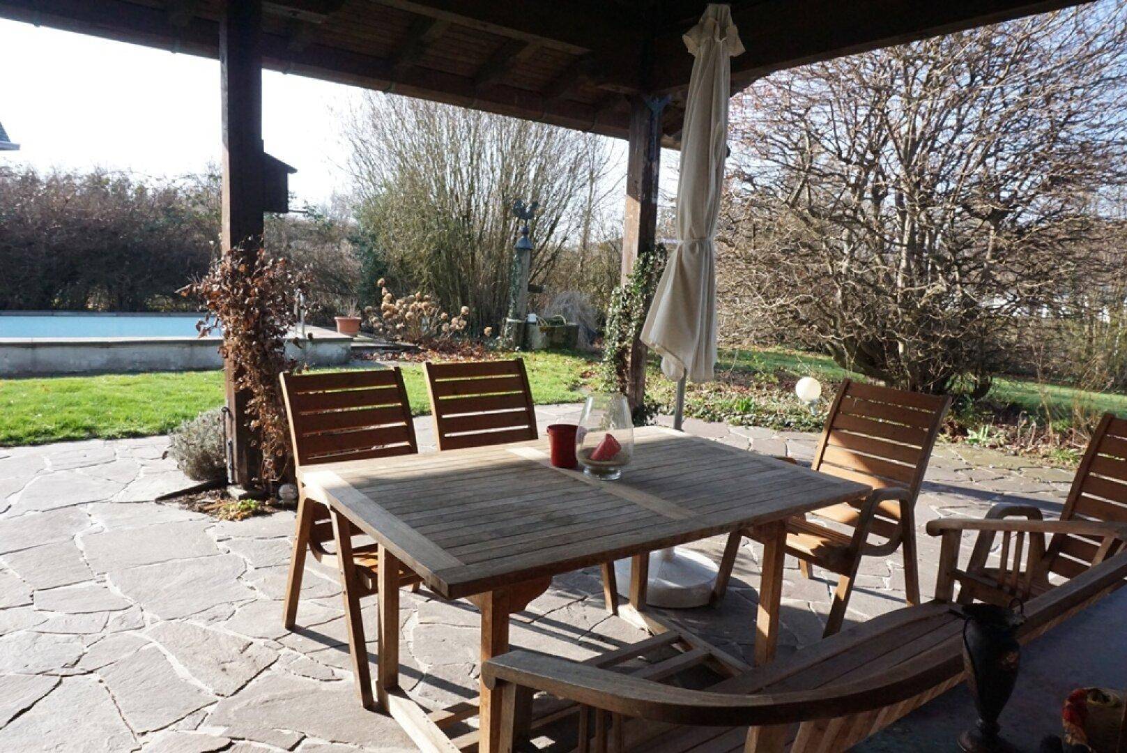 Überdachte Terrasse mit Holztisch und Stühlen, ideal für Mahlzeiten im Freien mit Poolblick.
