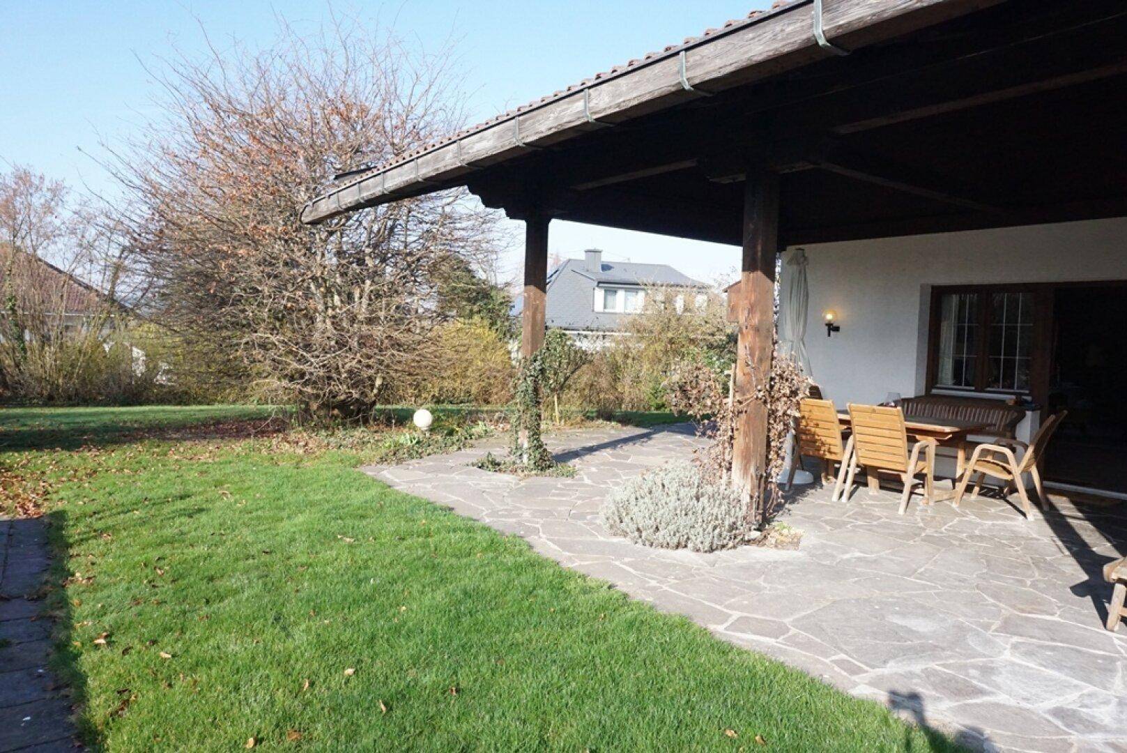 Geräumige überdachte Terrasse mit Steinboden und Zugang zum grünen Gartenbereich.
