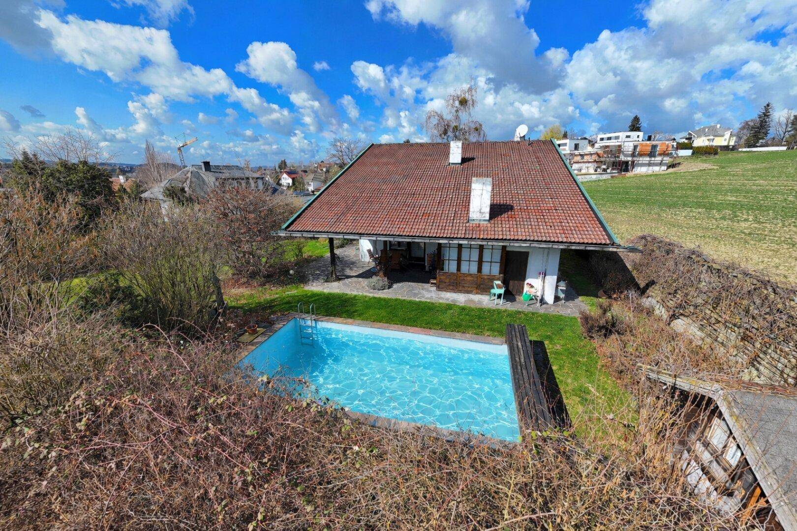 Haus mit rotem Ziegeldach und einem kleinen Pool im Garten, umgeben von Sträuchern.