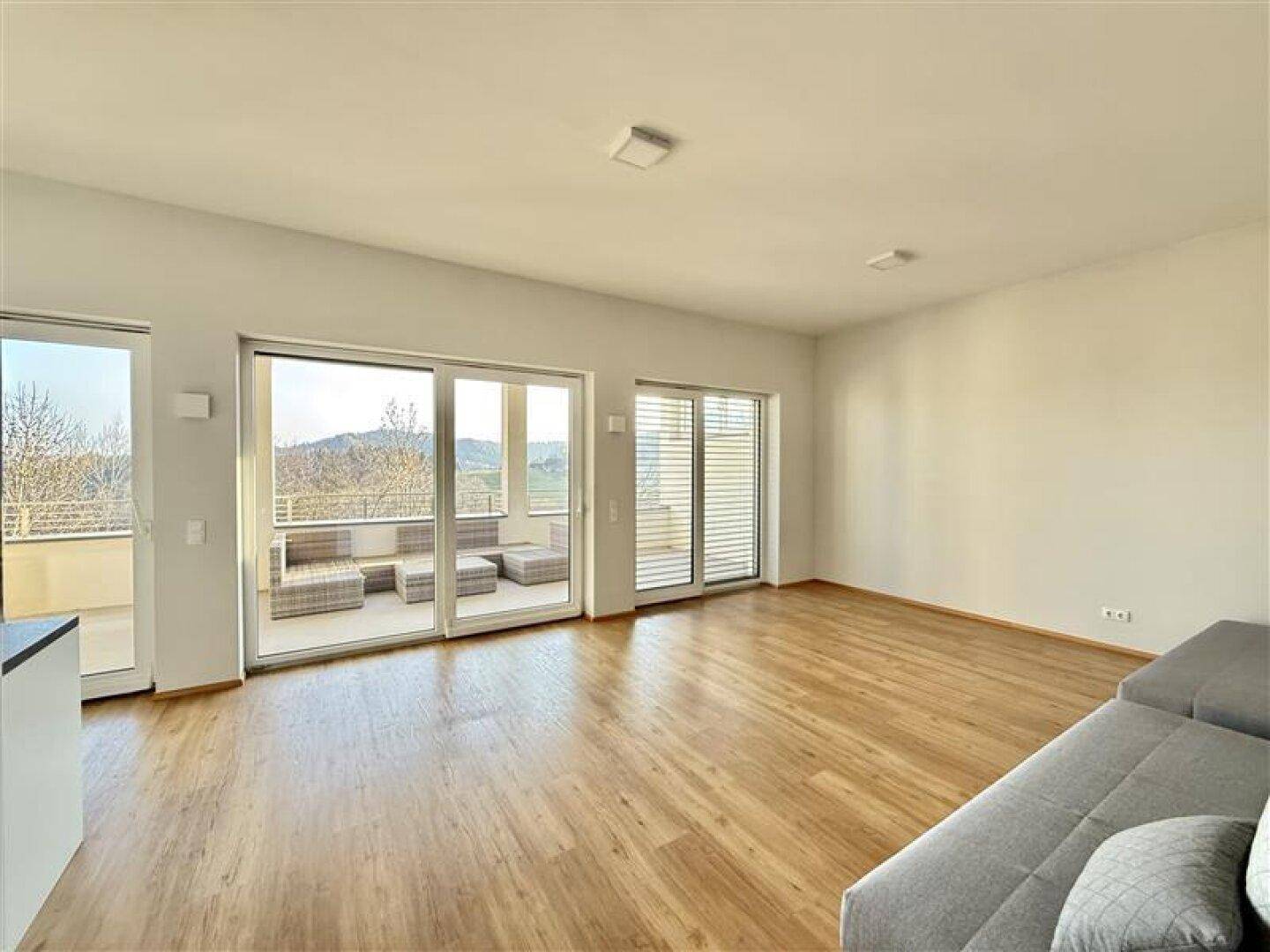 Helles Wohnzimmer mit Holzboden, großen Schiebetüren und Zugang zu einem Balkon mit Weitblick.